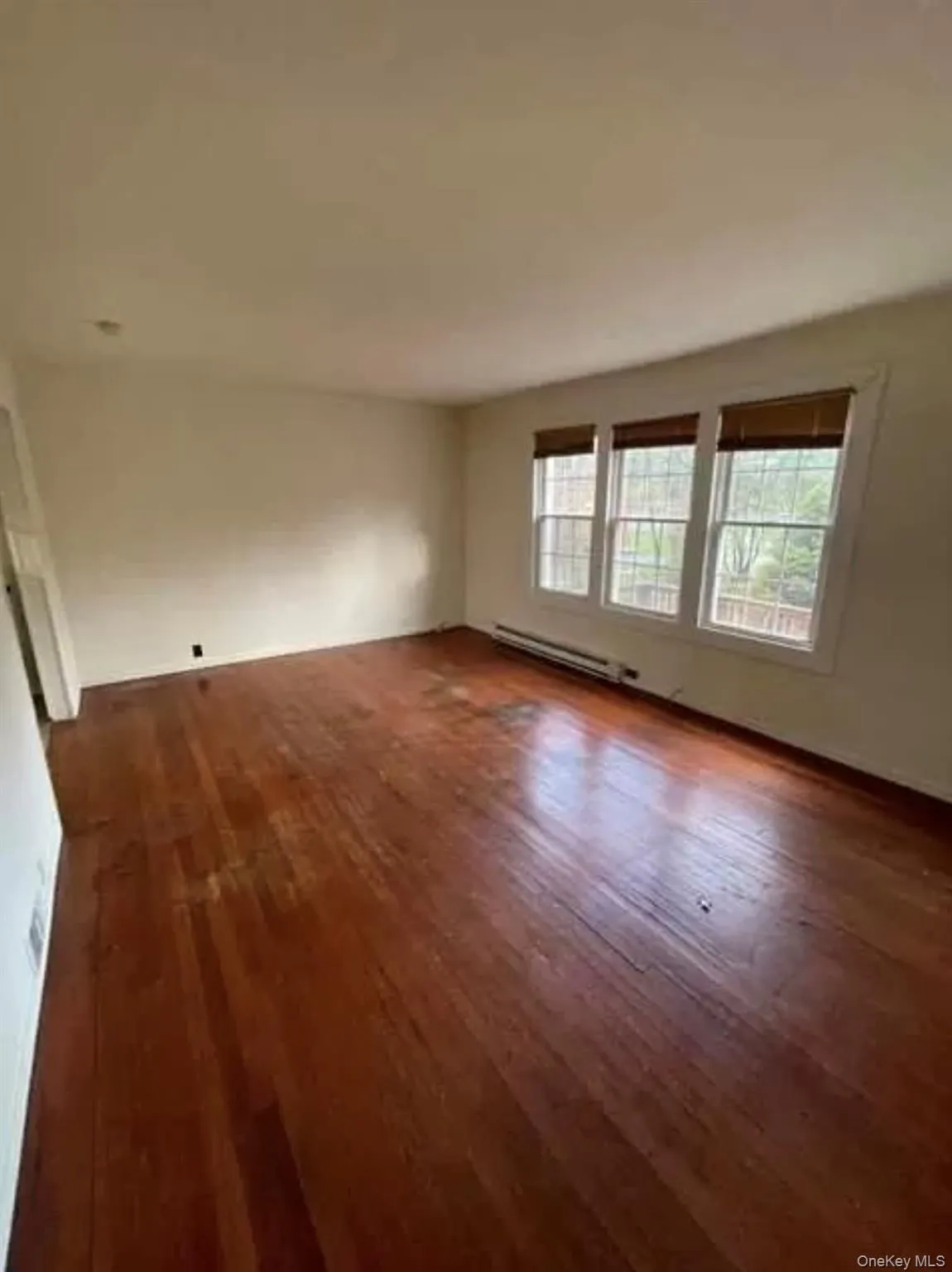 Unfurnished room featuring dark wood-style flooring and baseboard heating Unfurnished room featuring dark wood-style flooring and baseboard heating