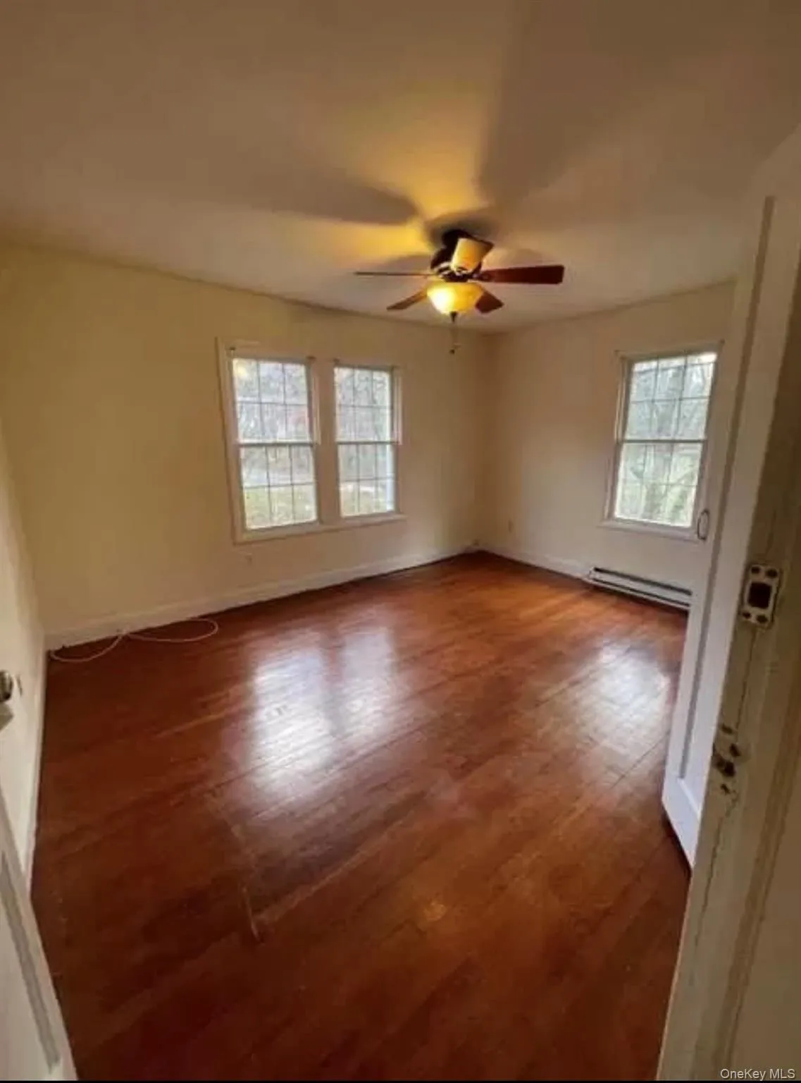 Empty room featuring wood finished floors, ceiling fan, and baseboard heating Empty room featuring wood finished floors, ceiling fan, and baseboard heating