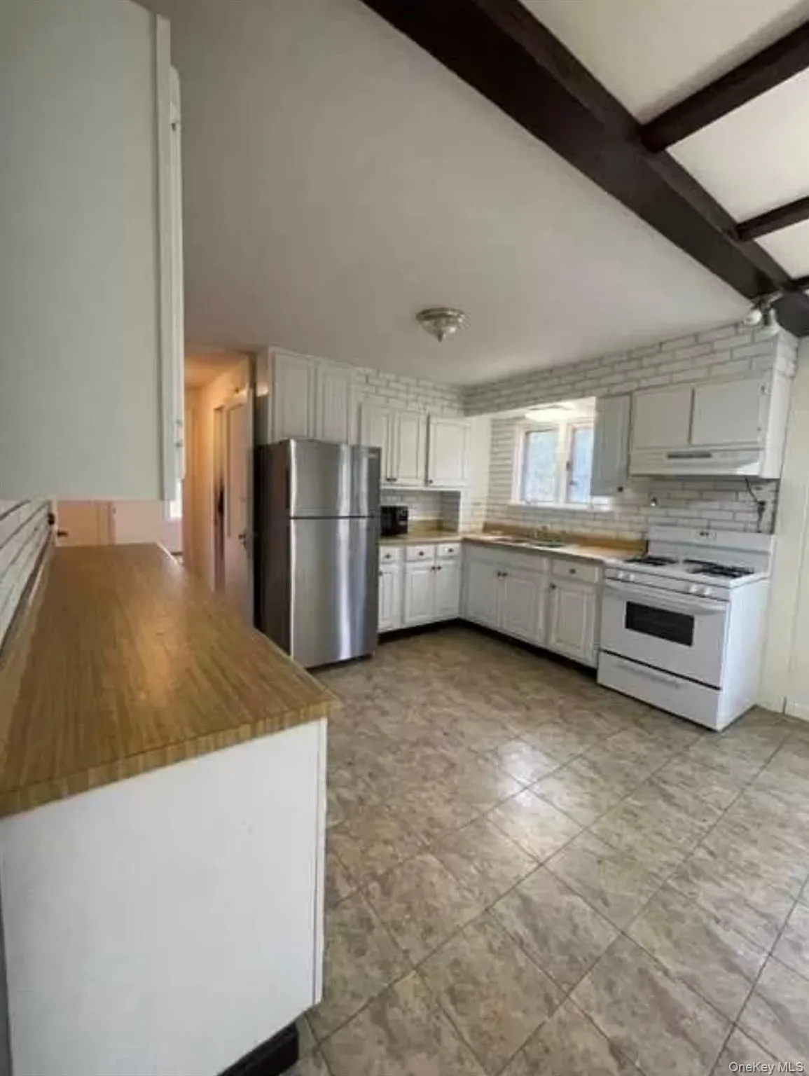 Kitchen with gas range gas stove, freestanding refrigerator, decorative backsplash, white cabinetry, and beam ceiling Kitchen with gas range gas stove, freestanding refrigerator, decorative backsplash, white cabinetry, and beam ceiling