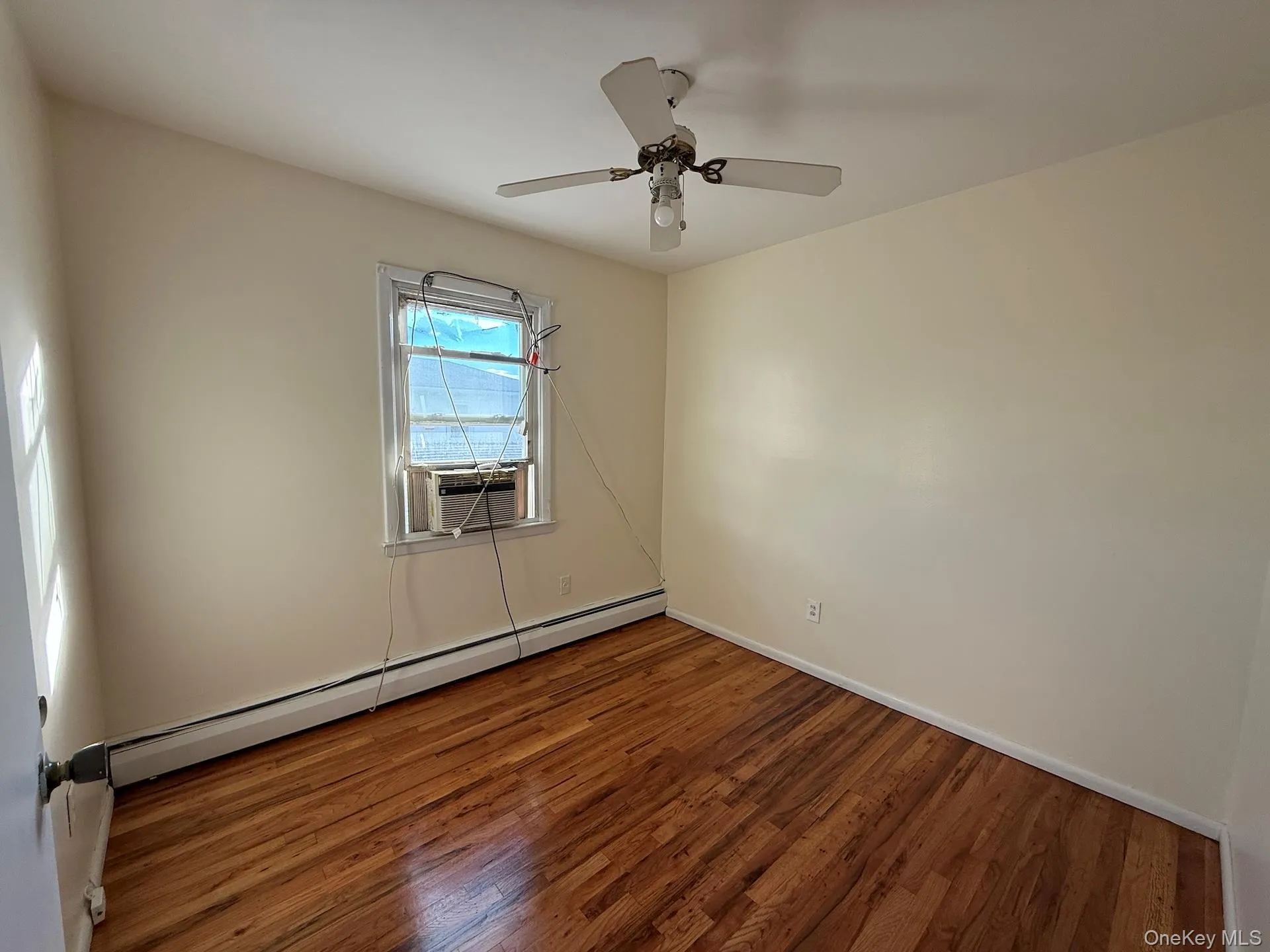 Empty room with a baseboard heating unit, wood finished floors, cooling unit, and ceiling fan Empty room with a baseboard heating unit, wood finished floors, cooling unit, and ceiling fan