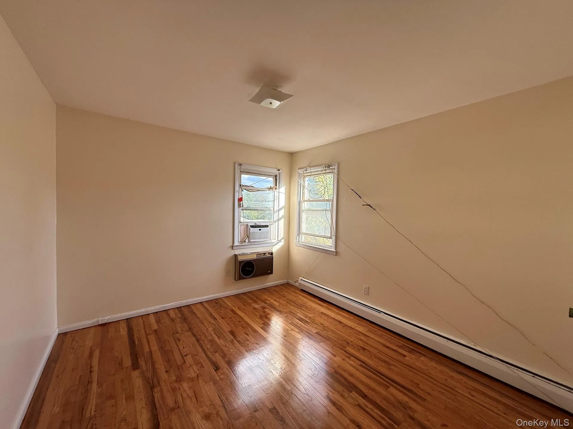 Spare room with baseboard heating, wood finished floors, and cooling unit Spare room with baseboard heating, wood finished floors, and cooling unit