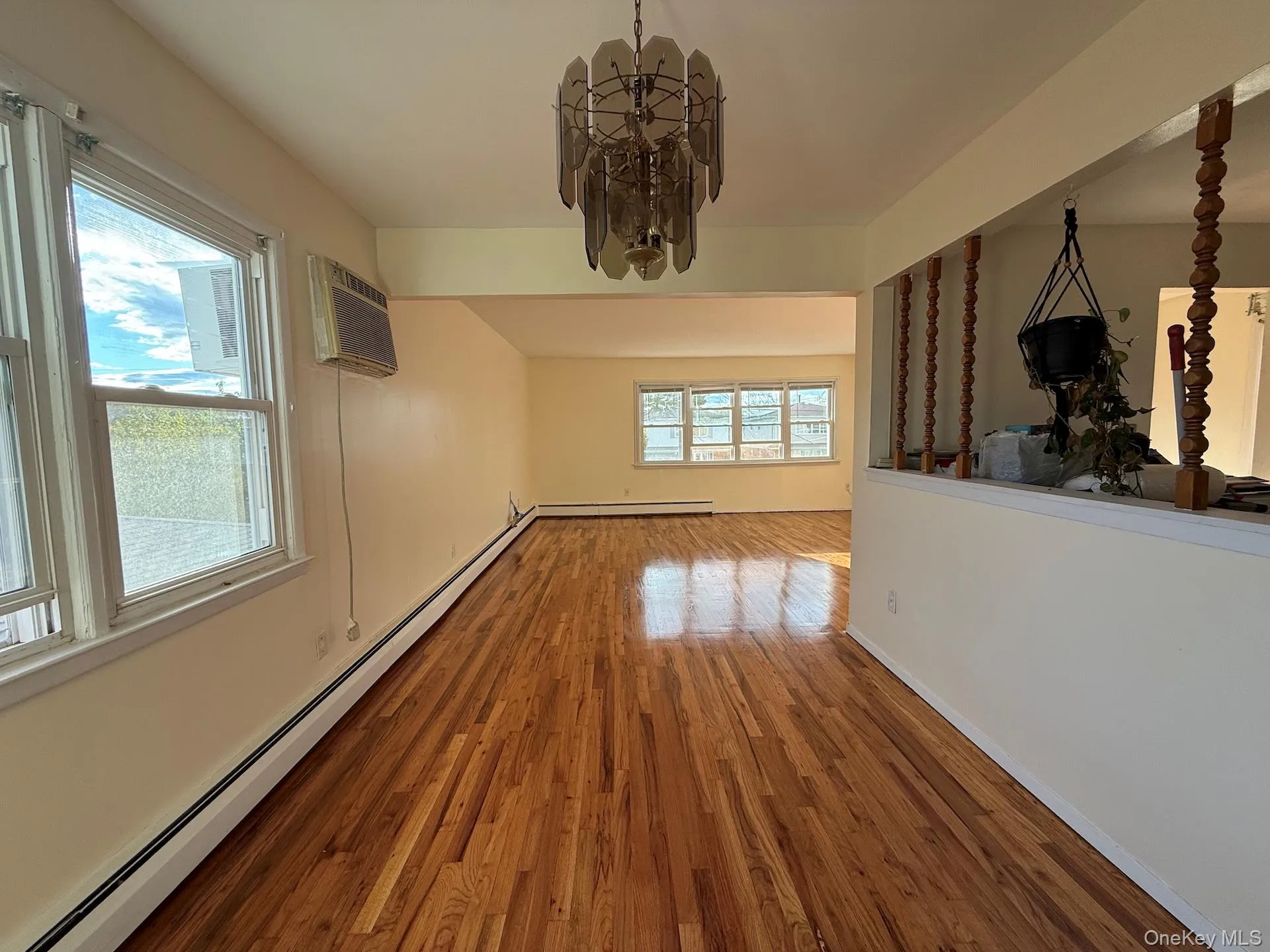 Unfurnished dining area with a baseboard radiator, a chandelier, wood finished floors, and an AC wall unit Unfurnished dining area with a baseboard radiator, a chandelier, wood finished floors, and an AC wall unit