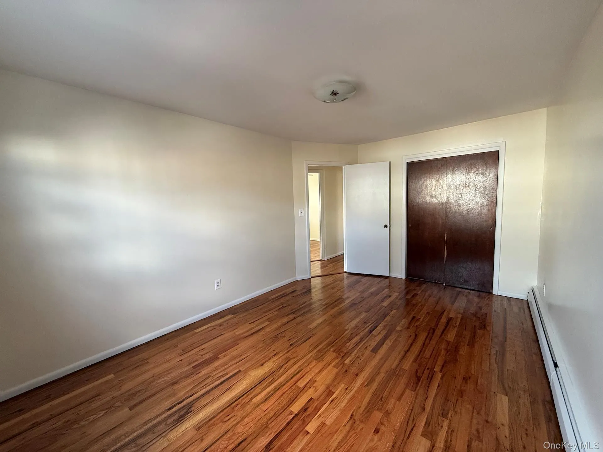 Unfurnished bedroom featuring a baseboard radiator, dark wood-style floors, and a closet Unfurnished bedroom featuring a baseboard radiator, dark wood-style floors, and a closet