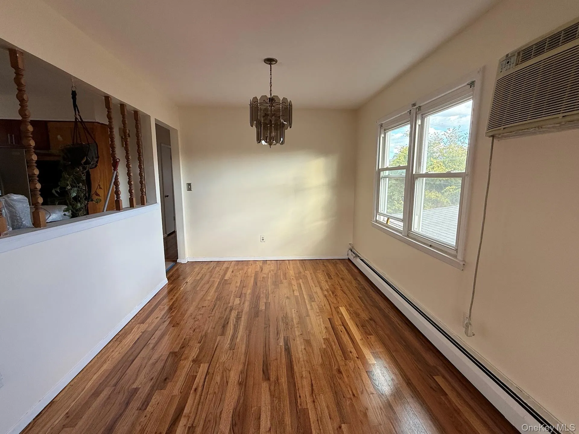 Unfurnished dining area with a baseboard heating unit, a chandelier, wood finished floors, and an AC wall unit Unfurnished dining area with a baseboard heating unit, a chandelier, wood finished floors, and an AC wall unit