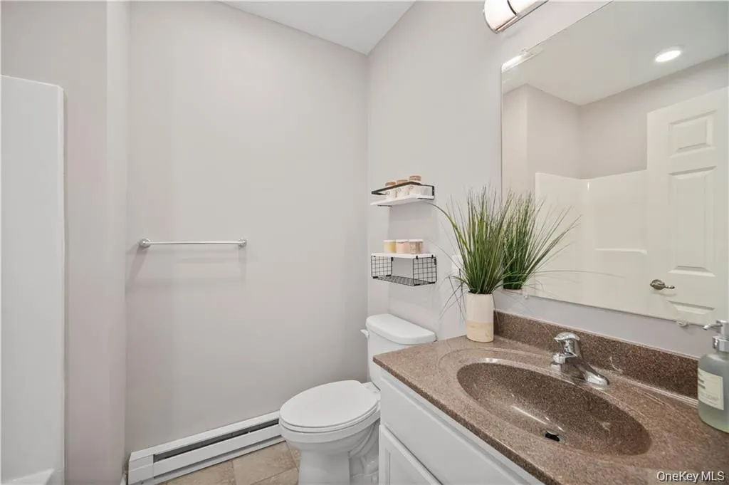 Half bathroom featuring baseboard heating, vanity, and light tile patterned flooring Half bathroom featuring baseboard heating, vanity, and light tile patterned flooring