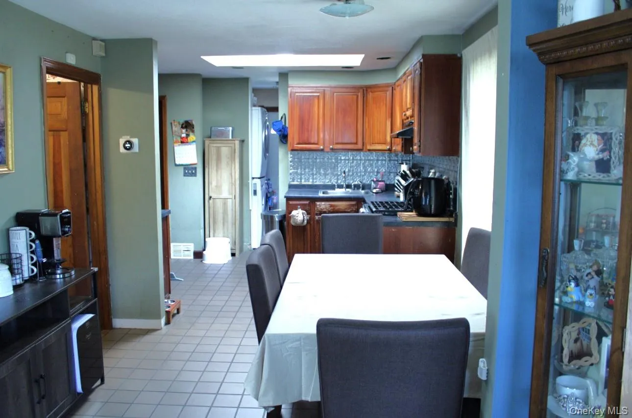 Kitchen with dark countertops, decorative backsplash, light tile patterned floors, brown cabinetry, and under cabinet range hood Kitchen with dark countertops, decorative backsplash, light tile patterned floors, brown cabinetry, and under cabinet range hood