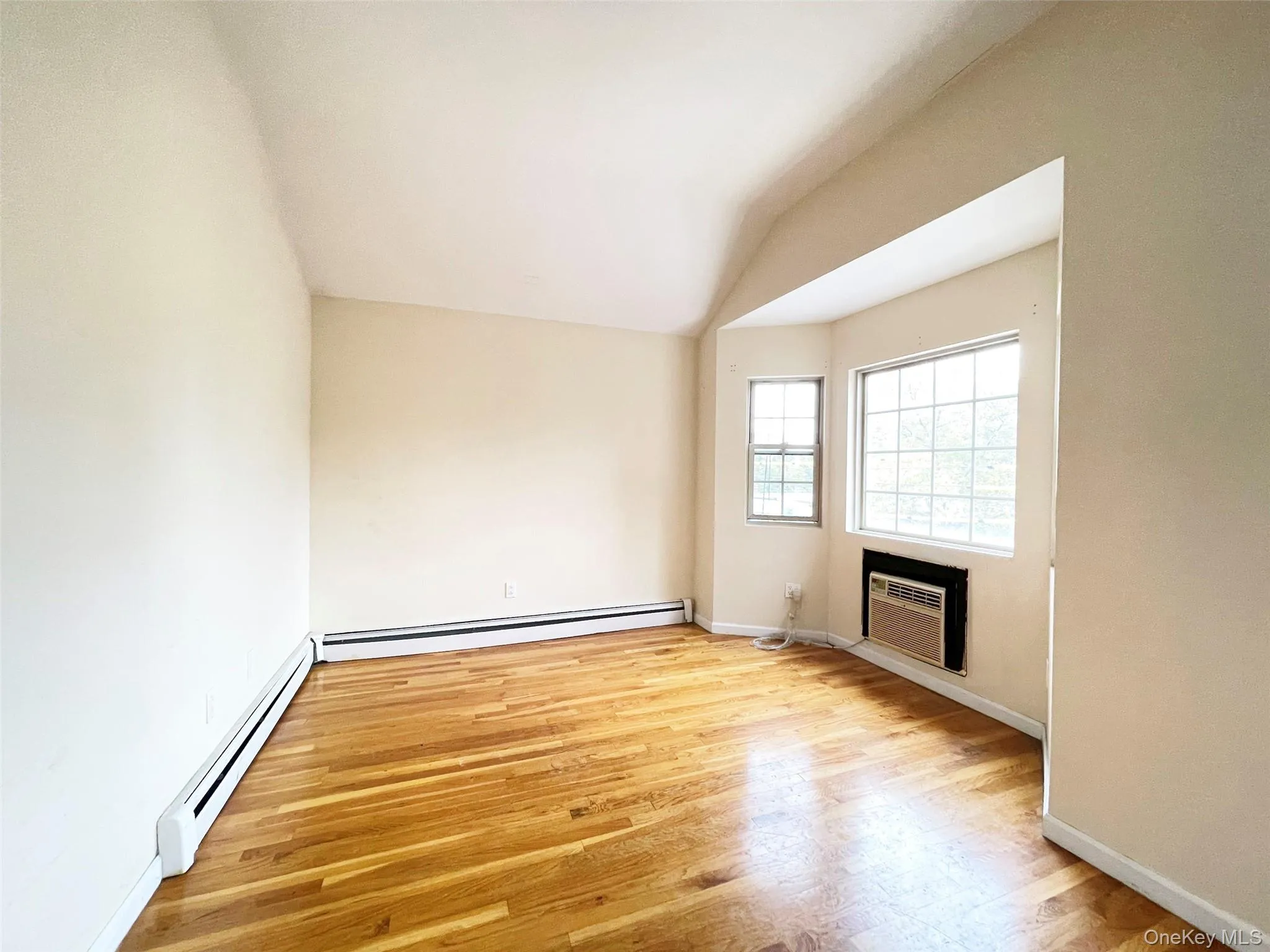 Unfurnished living room featuring a baseboard heating unit, lofted ceiling, light wood-style floors, and an AC wall unit Unfurnished living room featuring a baseboard heating unit, lofted ceiling, light wood-style floors, and an AC wall unit