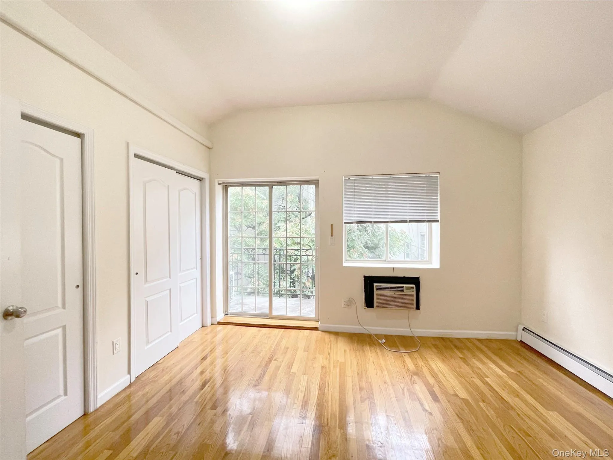 Unfurnished bedroom with light wood-style floors, vaulted ceiling, a closet, baseboard heating, and access to outside Unfurnished bedroom with light wood-style floors, vaulted ceiling, a closet, baseboard heating, and access to outside