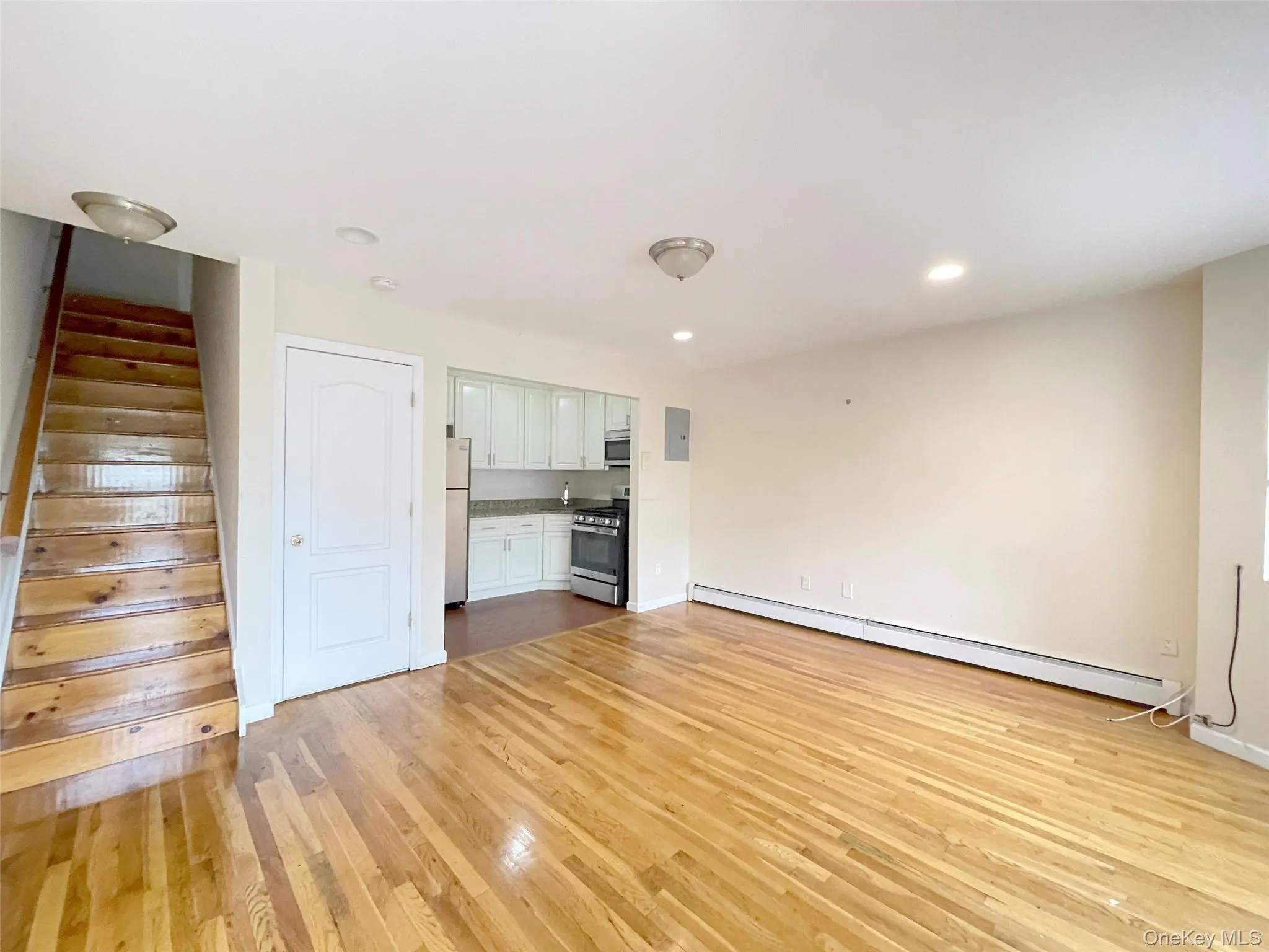 Unfurnished living room with stairway, light wood-style floors, a baseboard radiator, recessed lighting, and electric panel Unfurnished living room with stairway, light wood-style floors, a baseboard radiator, recessed lighting, and electric panel