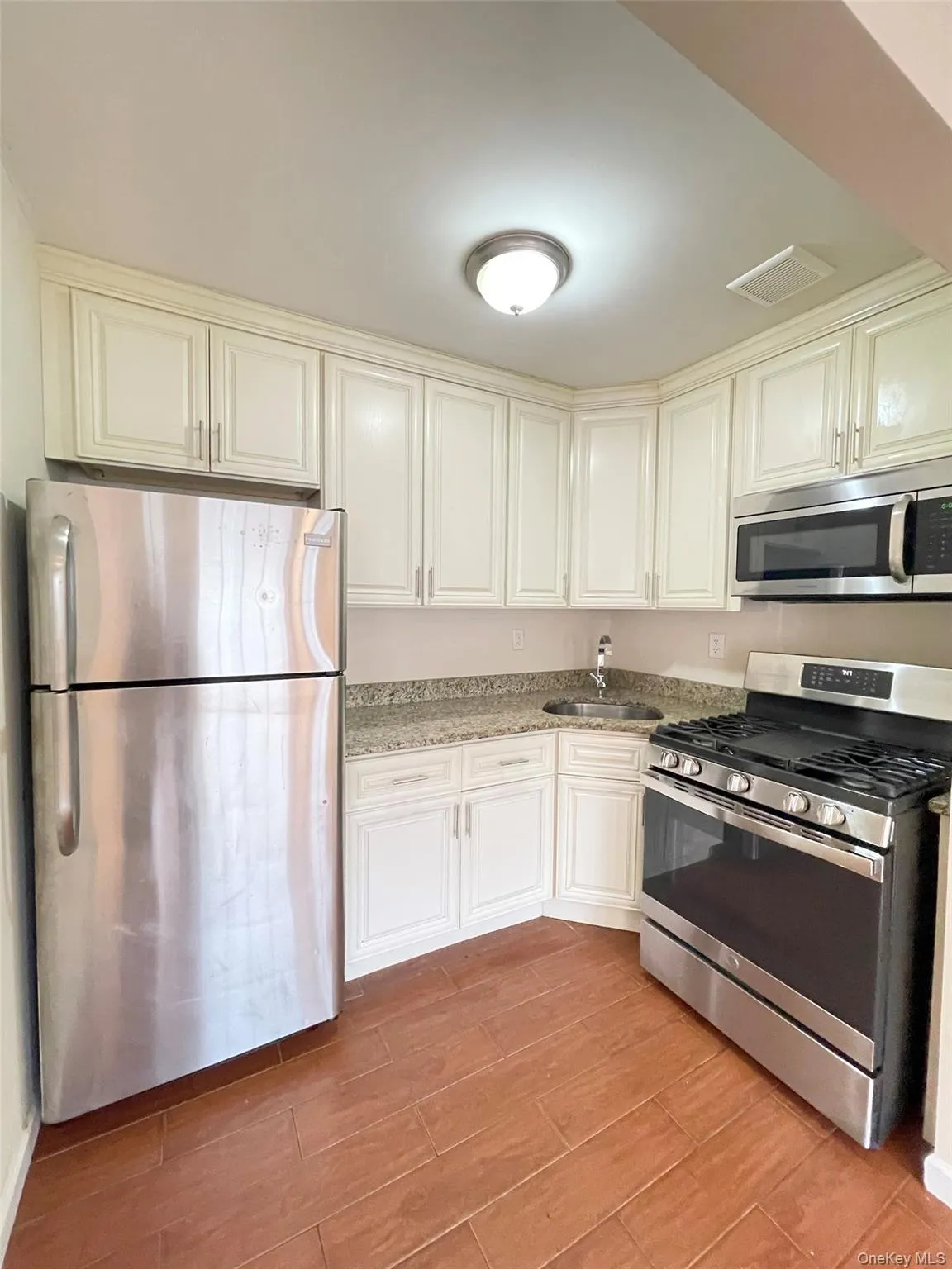 Kitchen with stainless steel appliances, light stone countertops, wood tiled floors, and white cabinetry Kitchen with stainless steel appliances, light stone countertops, wood tiled floors, and white cabinetry