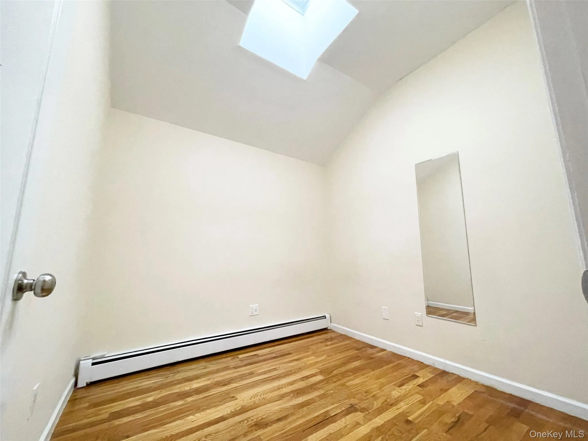 Spare room with a skylight, lofted ceiling, wood finished floors, and a baseboard heating unit Spare room with a skylight, lofted ceiling, wood finished floors, and a baseboard heating unit