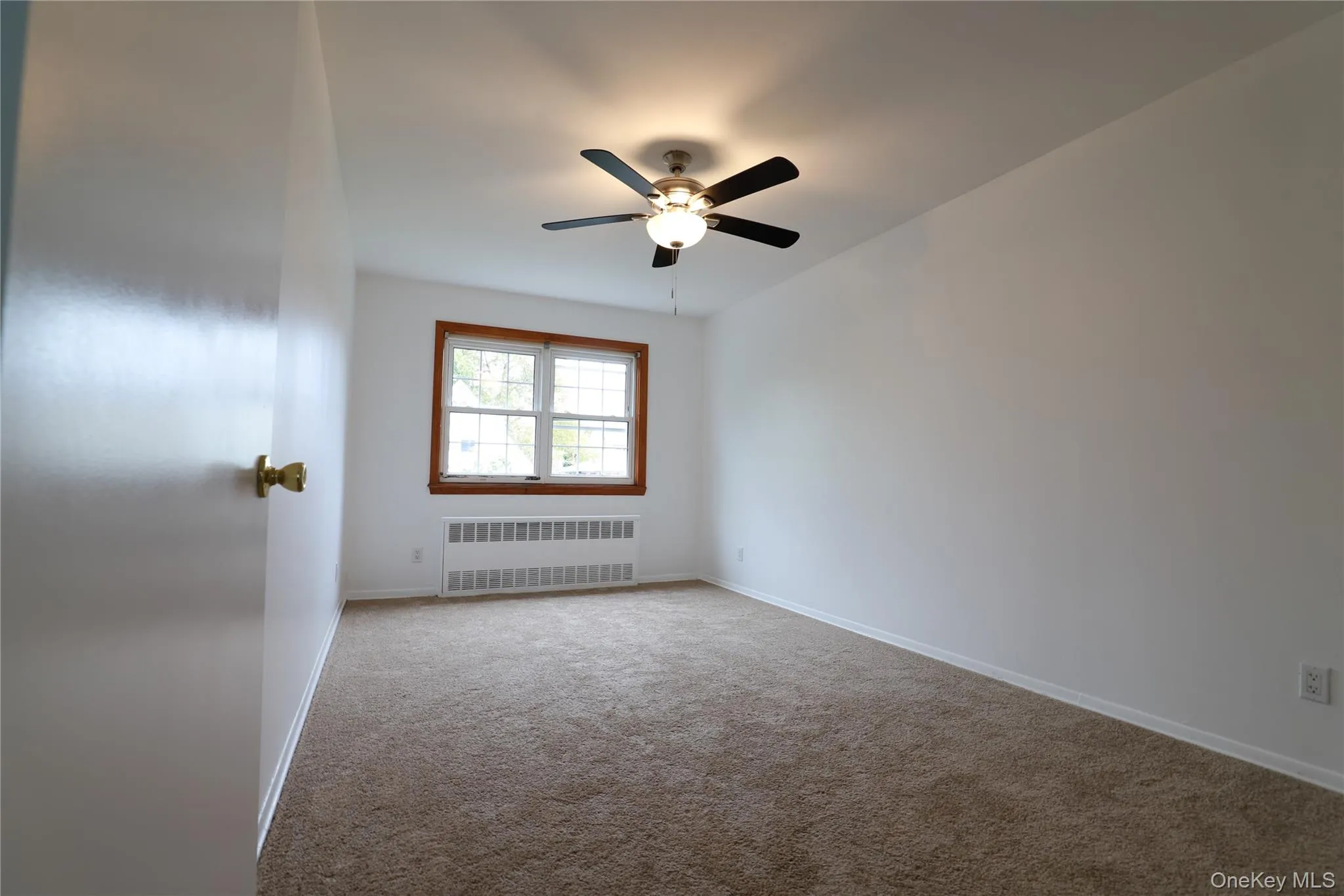 Bedroom featuring light carpet, radiator heating unit, and a ceiling fan Bedroom featuring light carpet, radiator heating unit, and a ceiling fan