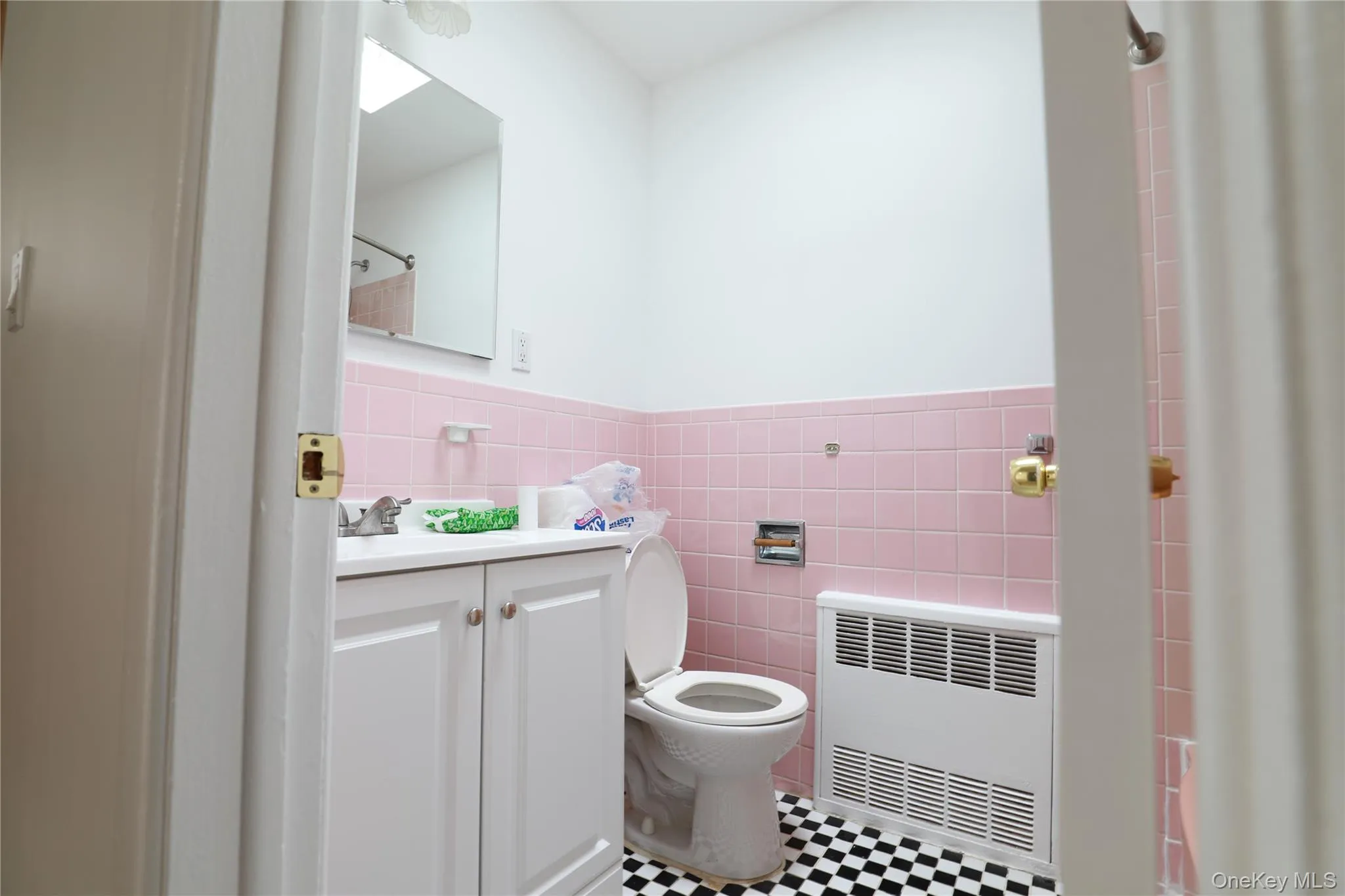 Bathroom with tile walls, vanity, radiator heating unit, a shower with curtain, and a wainscoted wall Bathroom with tile walls, vanity, radiator heating unit, a shower with curtain, and a wainscoted wall