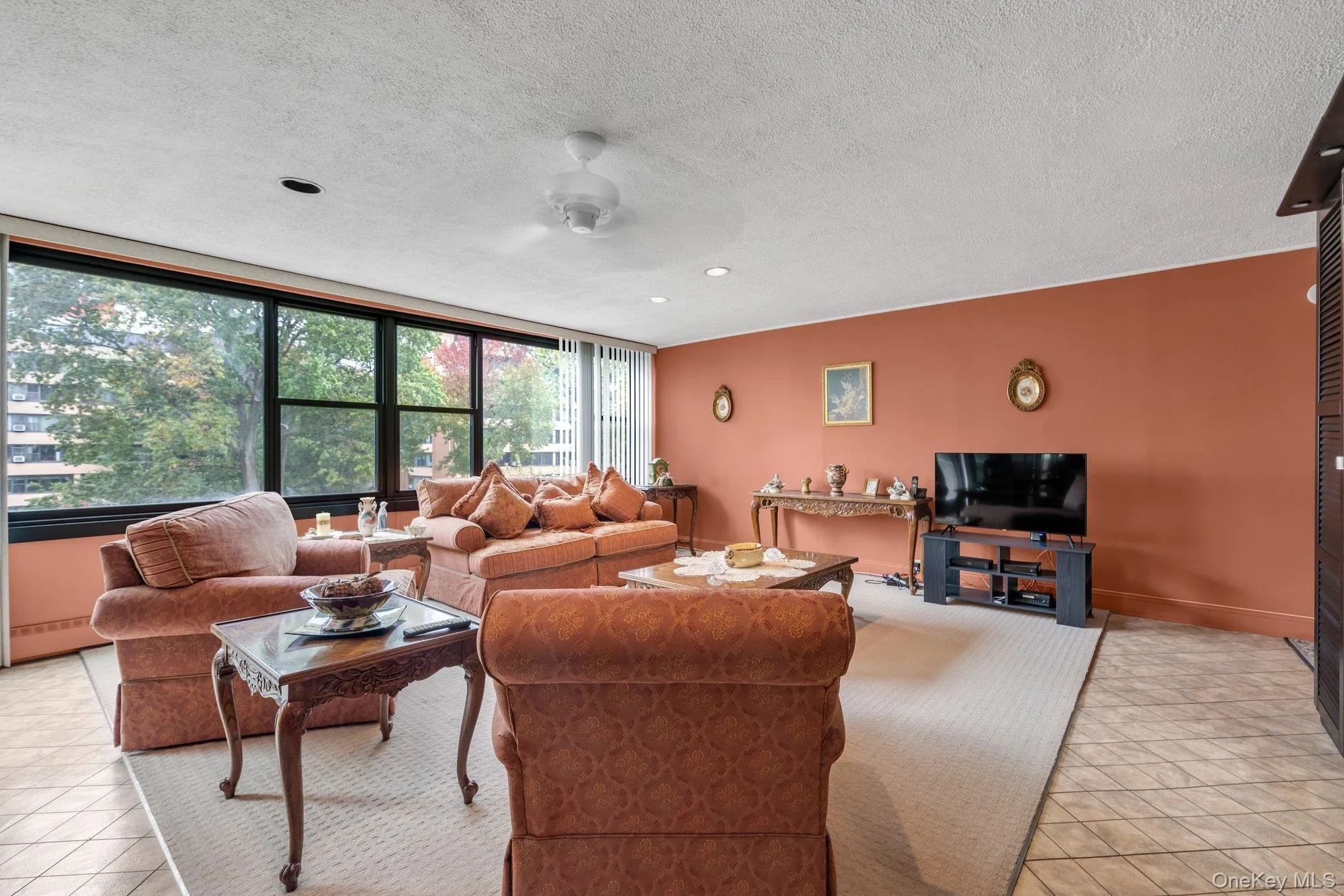 Living area featuring light tile patterned floors, a textured ceiling, a baseboard radiator, and a ceiling fan Living area featuring light tile patterned floors, a textured ceiling, a baseboard radiator, and a ceiling fan