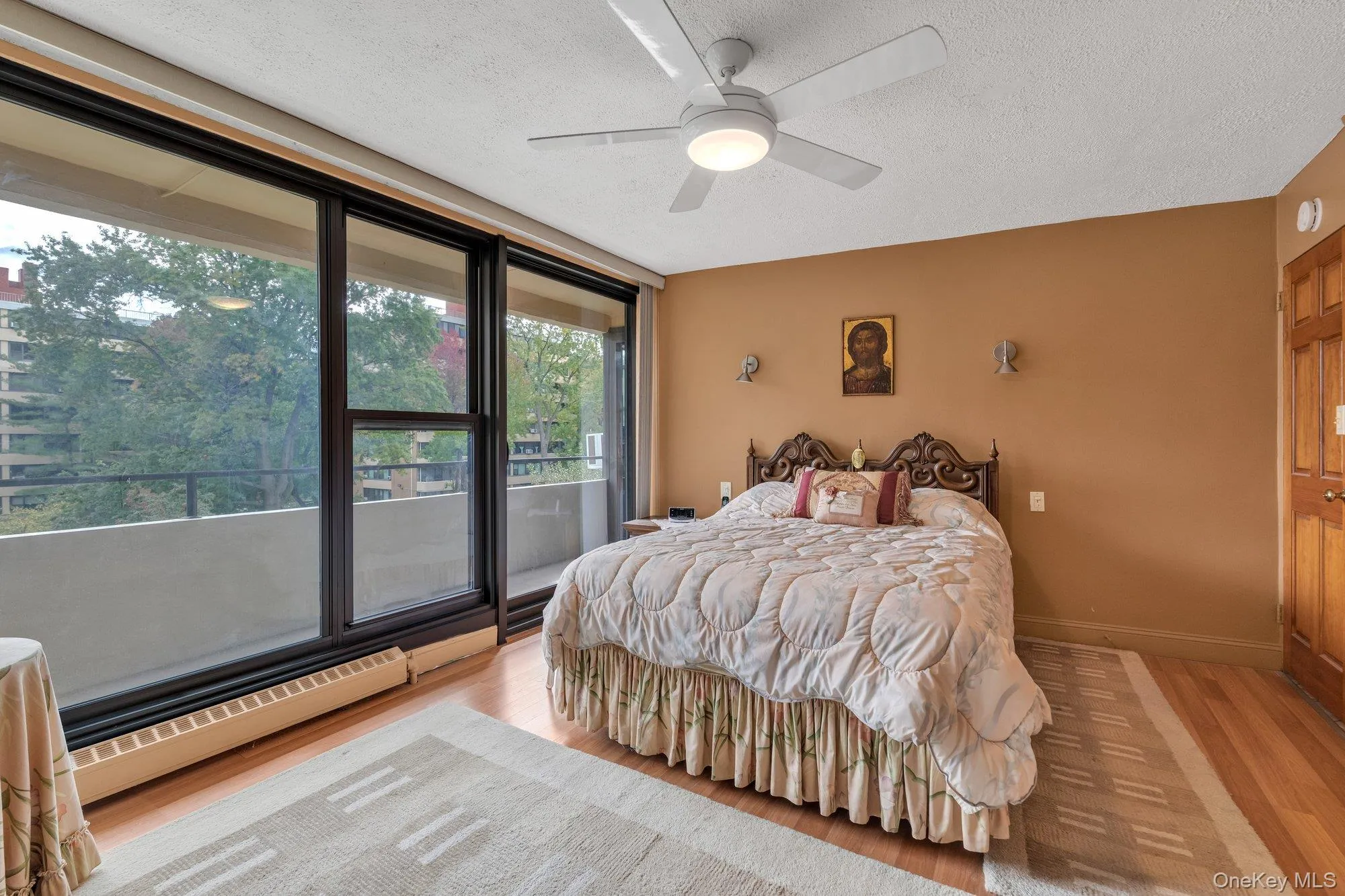 Bedroom featuring a textured ceiling, a baseboard heating unit, wood finished floors, access to outside, and a ceiling fan Bedroom featuring a textured ceiling, a baseboard heating unit, wood finished floors, access to outside, and a ceiling fan