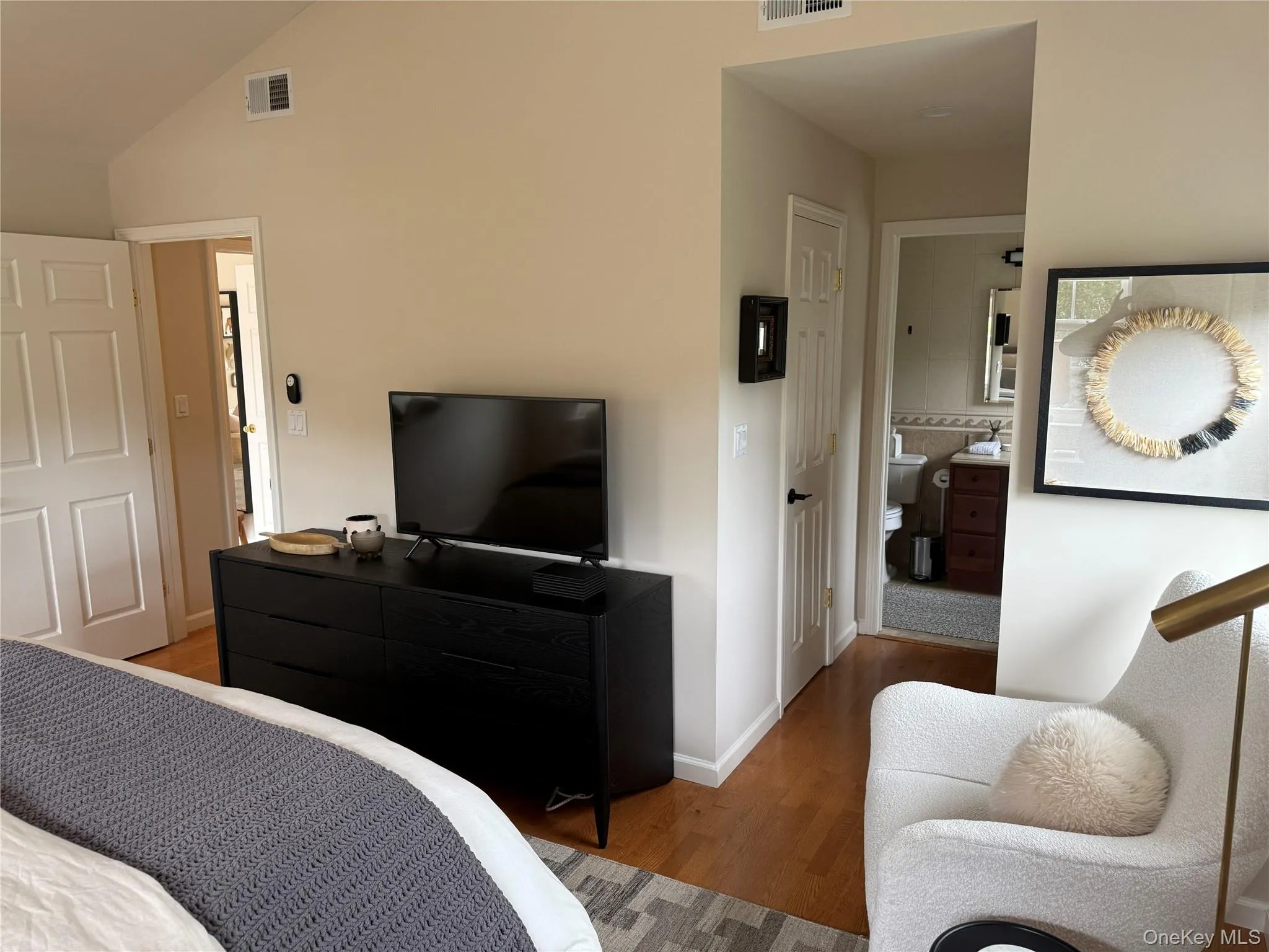 Bedroom featuring wood finished floors, vaulted ceiling, and ensuite bath Bedroom featuring wood finished floors, vaulted ceiling, and ensuite bath
