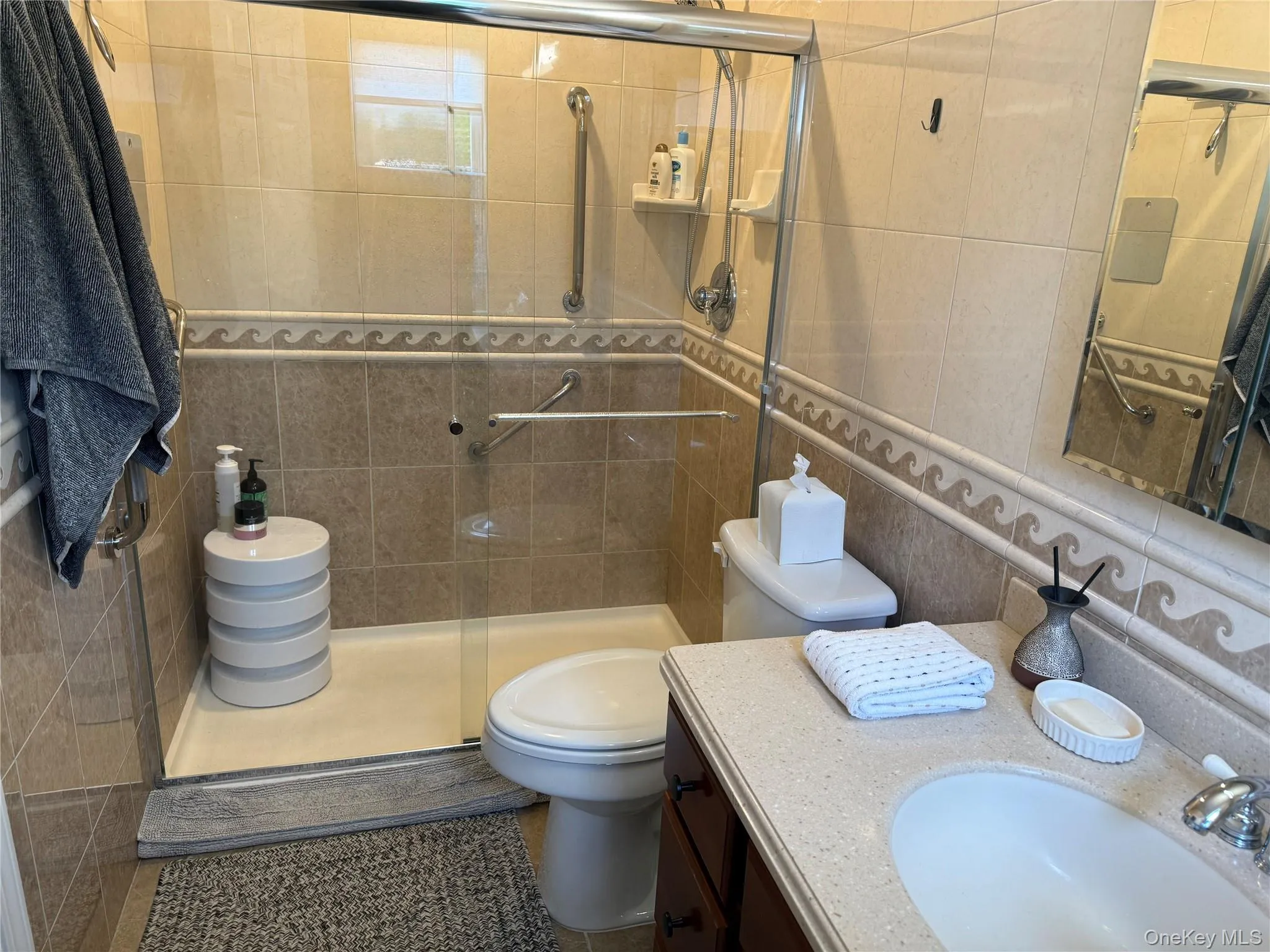 Bathroom featuring tile walls, a shower stall, vanity, and dark tile patterned flooring Bathroom featuring tile walls, a shower stall, vanity, and dark tile patterned flooring