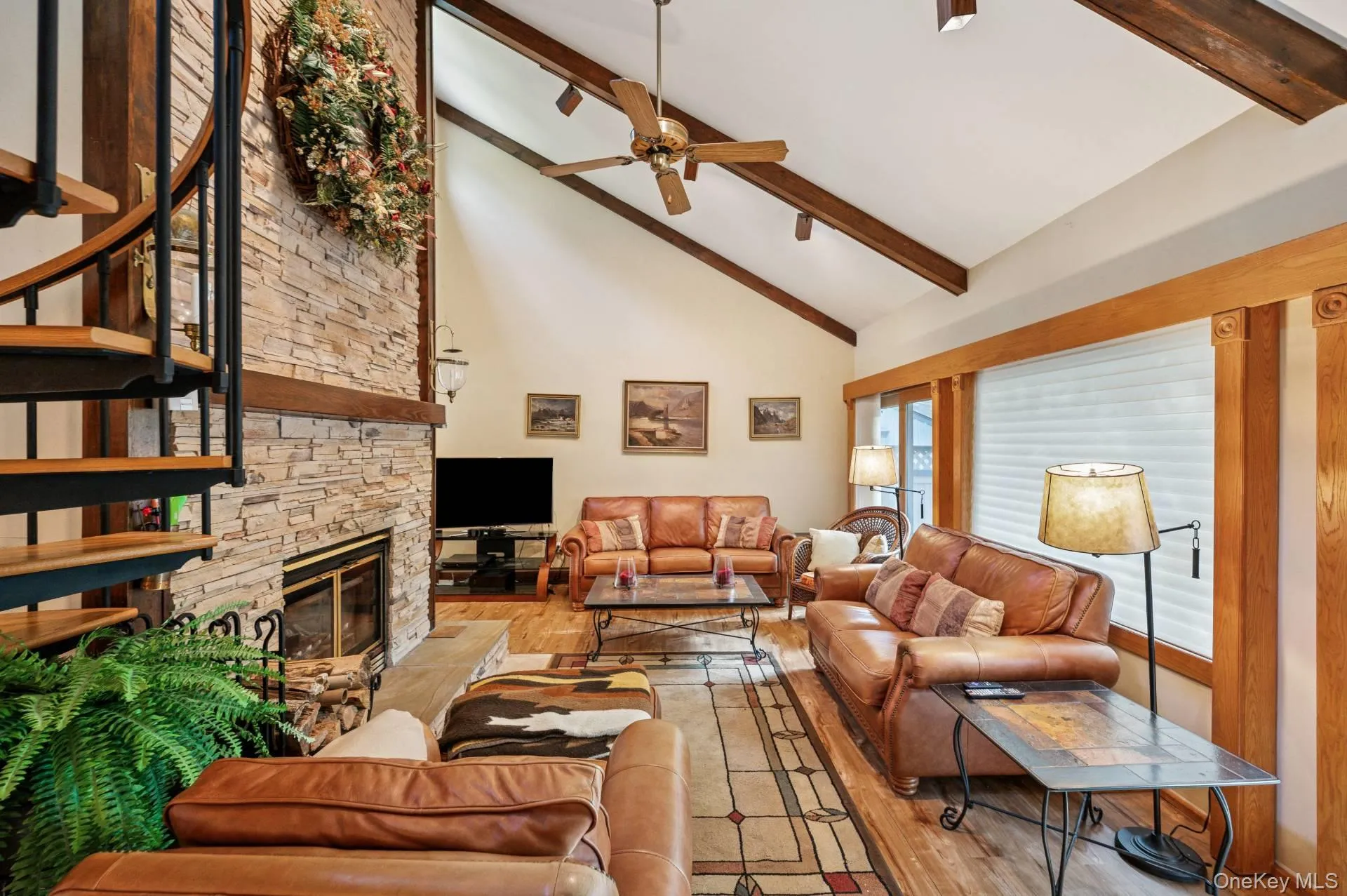 Living area featuring light wood-type flooring, beamed ceiling, high vaulted ceiling, a fireplace, and a ceiling fan Living area featuring light wood-type flooring, beamed ceiling, high vaulted ceiling, a fireplace, and a ceiling fan