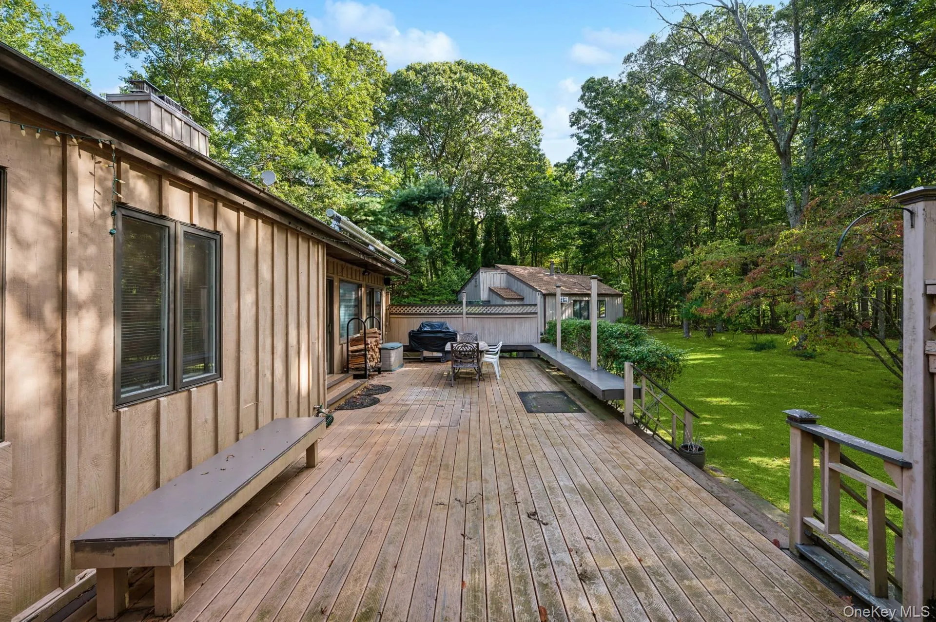 Wooden deck featuring a lawn, outdoor dining area, and view of wooded area Wooden deck featuring a lawn, outdoor dining area, and view of wooded area