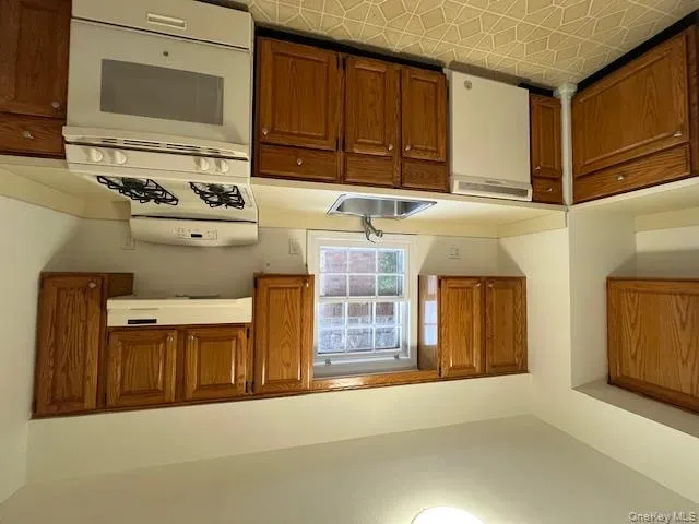 Kitchen with stove, brown cabinetry, light countertops, and dishwashing machine Kitchen with stove, brown cabinetry, light countertops, and dishwashing machine
