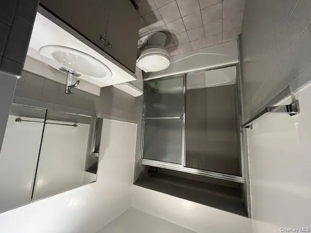 Bathroom featuring tile walls, shower / bath combination with glass door, vanity, wainscoting, and light tile patterned floors Bathroom featuring tile walls, shower / bath combination with glass door, vanity, wainscoting, and light tile patterned floors