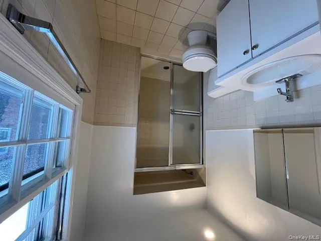 Full bathroom with tile walls, vanity, a shower stall, a wainscoted wall, and light tile patterned floors Full bathroom with tile walls, vanity, a shower stall, a wainscoted wall, and light tile patterned floors