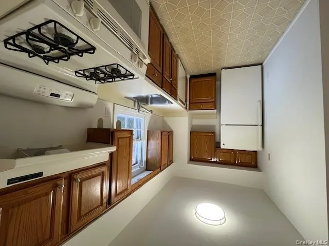 Kitchen featuring range, white fridge, extractor fan, light countertops, and brown cabinetry Kitchen featuring range, white fridge, extractor fan, light countertops, and brown cabinetry