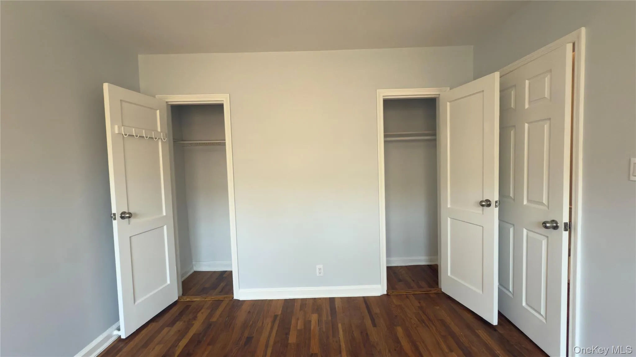 Unfurnished bedroom with dark wood-type flooring and two closets Unfurnished bedroom with dark wood-type flooring and two closets