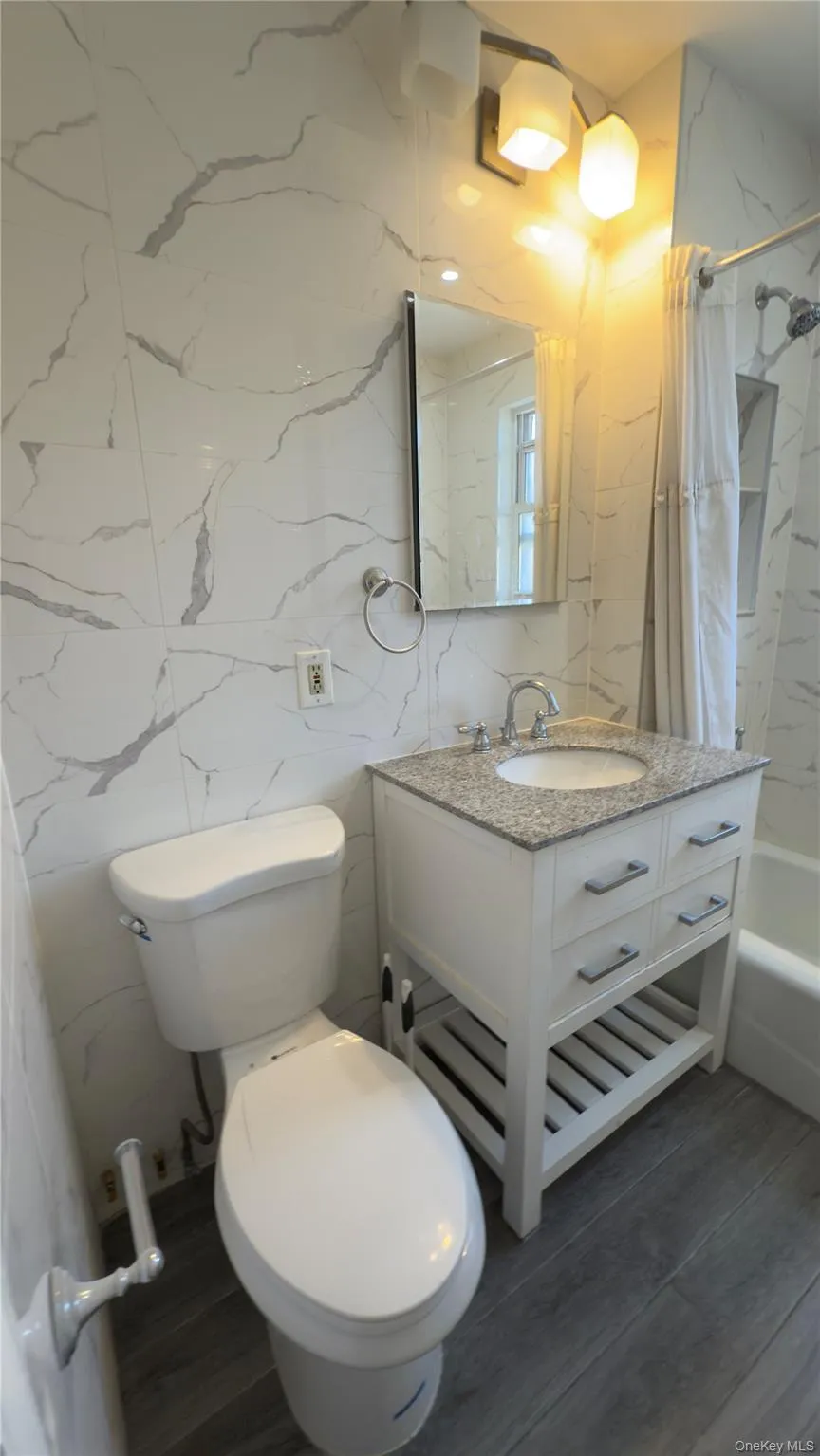 Bathroom featuring shower / bathtub combination with curtain, vanity, tile walls, and dark wood finished floors Bathroom featuring shower / bathtub combination with curtain, vanity, tile walls, and dark wood finished floors