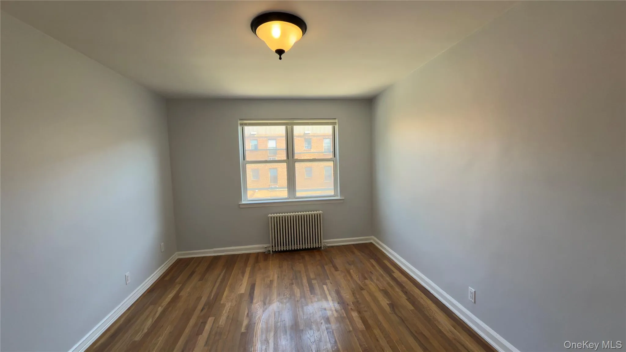 Unfurnished room featuring radiator and dark wood finished floors Unfurnished room featuring radiator and dark wood finished floors