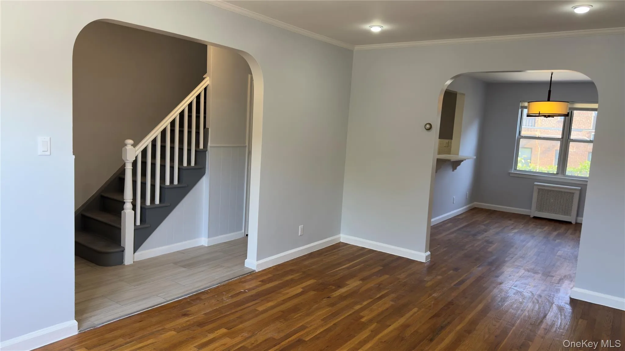 Unfurnished room featuring dark wood-type flooring, ornamental molding, stairway, and radiator Unfurnished room featuring dark wood-type flooring, ornamental molding, stairway, and radiator