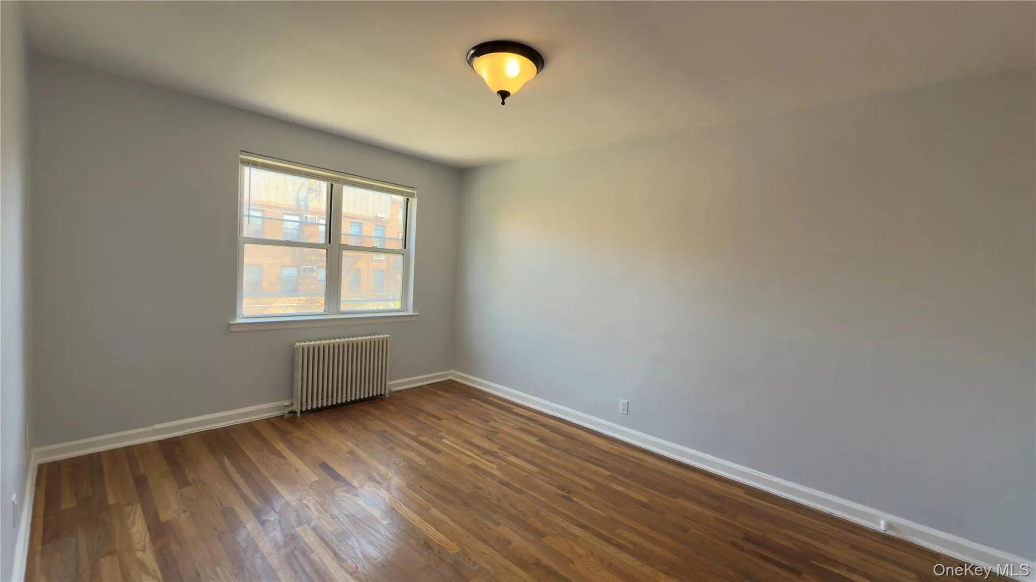 Empty room featuring radiator heating unit and dark wood-style flooring Empty room featuring radiator heating unit and dark wood-style flooring