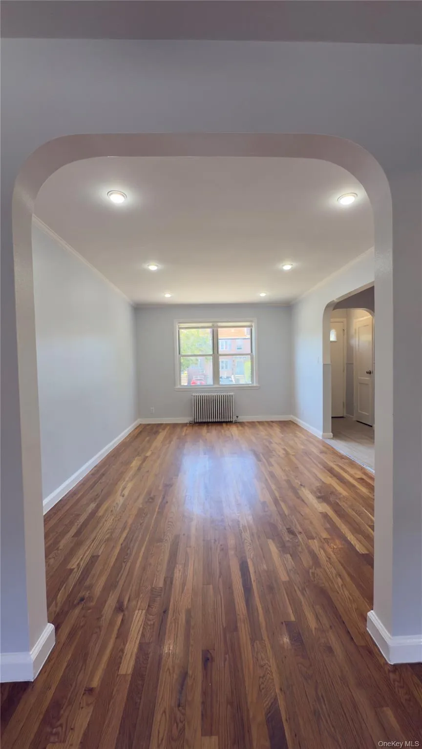Spare room with arched walkways, dark wood-style flooring, radiator, ornamental molding, and recessed lighting Spare room with arched walkways, dark wood-style flooring, radiator, ornamental molding, and recessed lighting