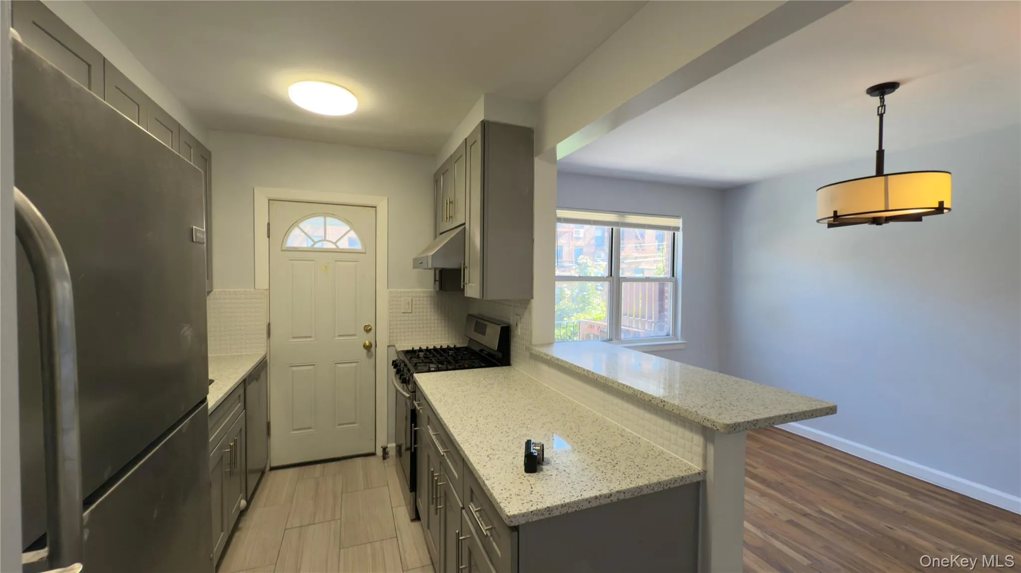 Kitchen featuring gray cabinets, appliances with stainless steel finishes, light stone countertops, backsplash, and hanging light fixtures Kitchen featuring gray cabinets, appliances with stainless steel finishes, light stone countertops, backsplash, and hanging light fixtures