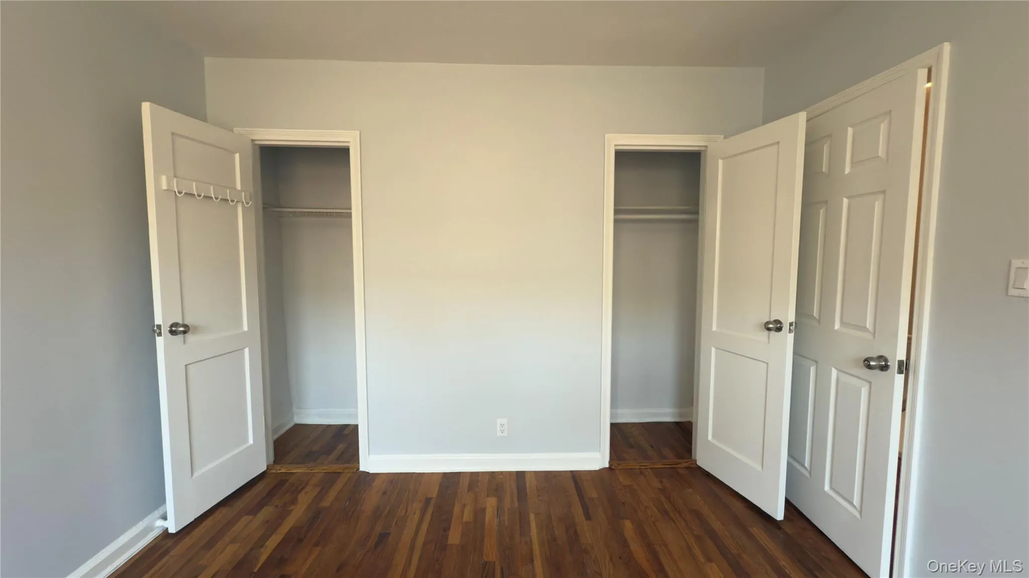 Unfurnished bedroom with dark wood-style floors and two closets Unfurnished bedroom with dark wood-style floors and two closets