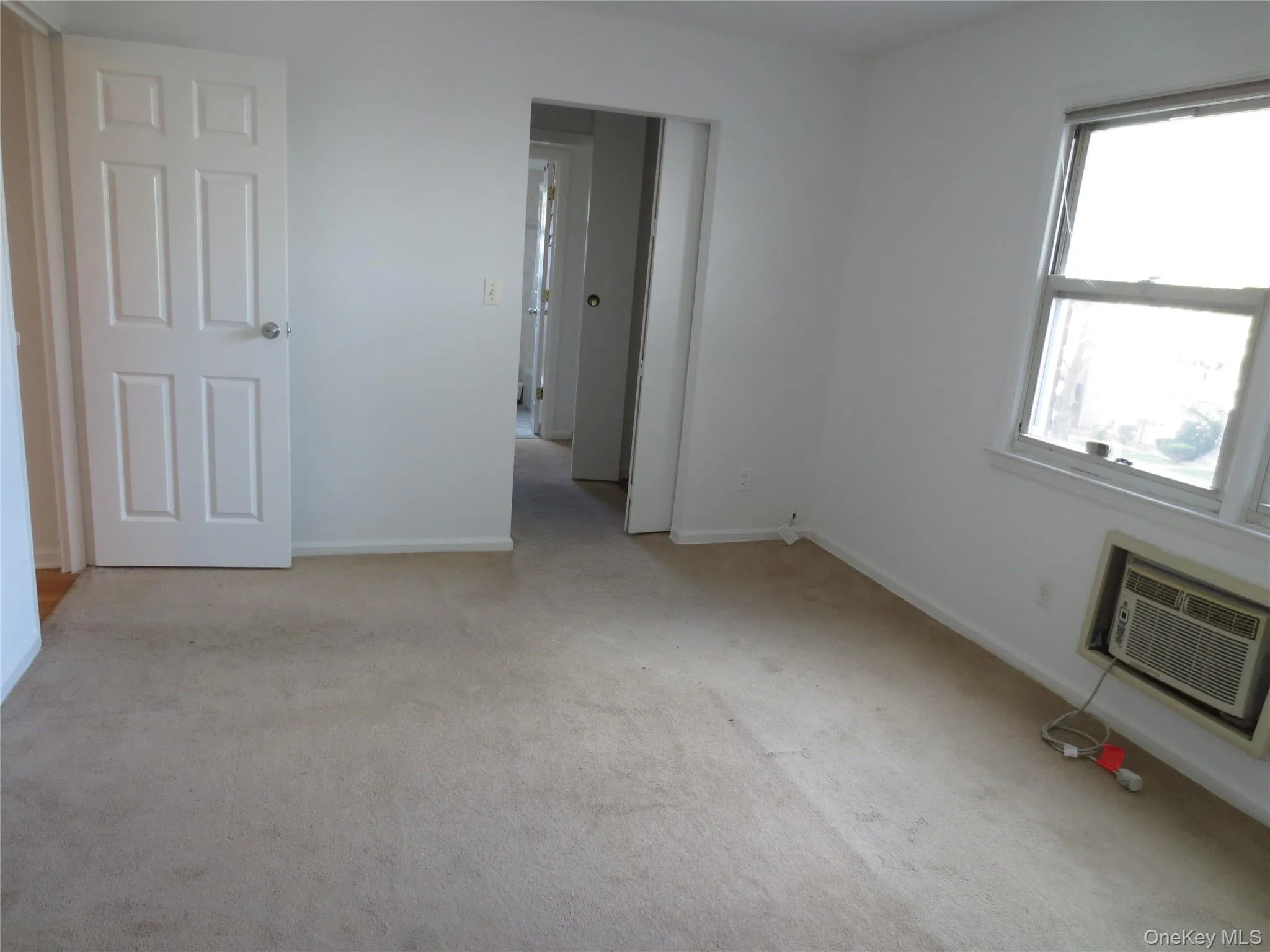 Unfurnished bedroom featuring light colored carpet and a wall mounted air conditioner Unfurnished bedroom featuring light colored carpet and a wall mounted air conditioner