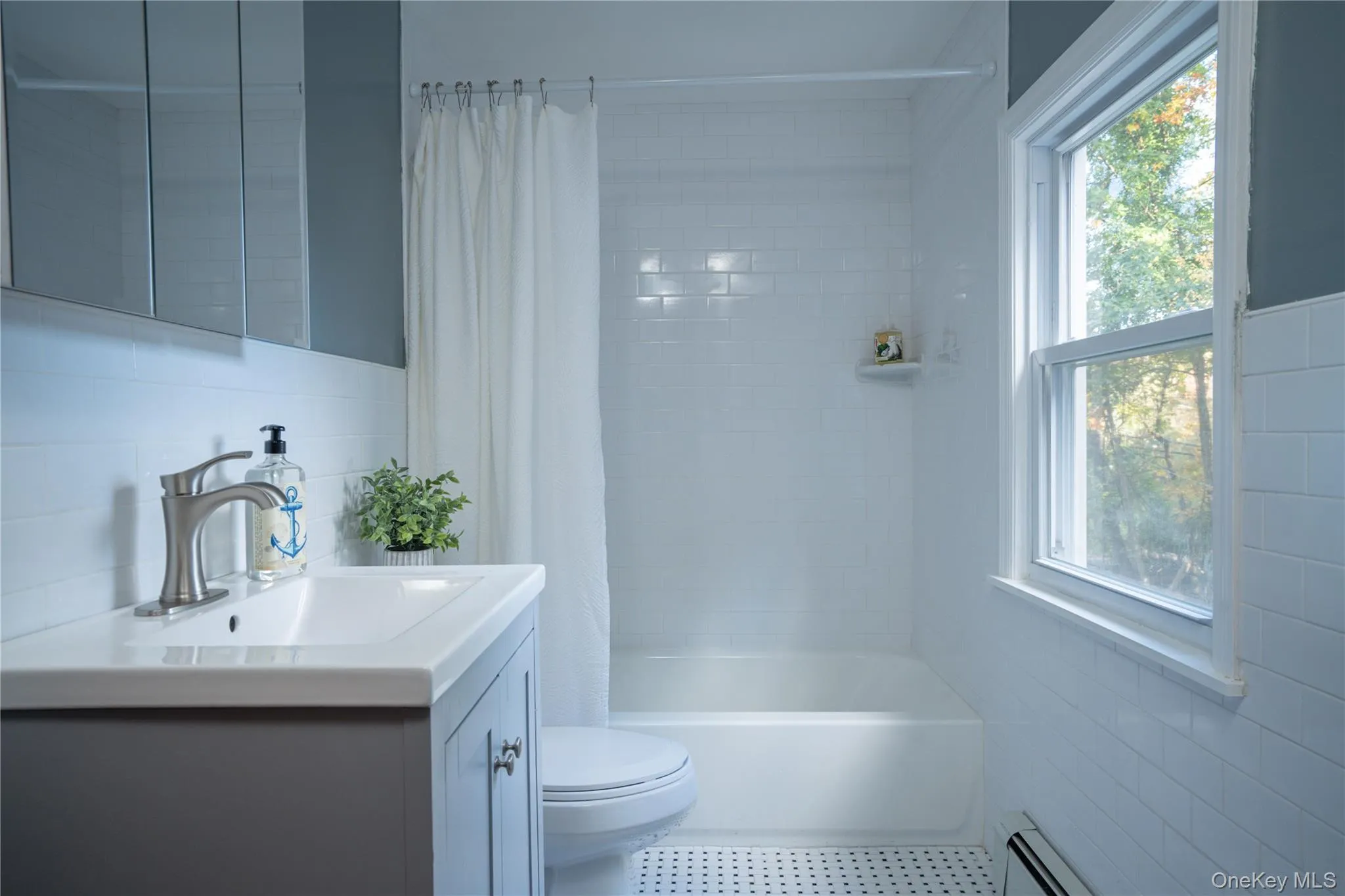 Bathroom with tile walls, vanity, shower / bathtub combination with curtain, a baseboard radiator, and backsplash Bathroom with tile walls, vanity, shower / bathtub combination with curtain, a baseboard radiator, and backsplash