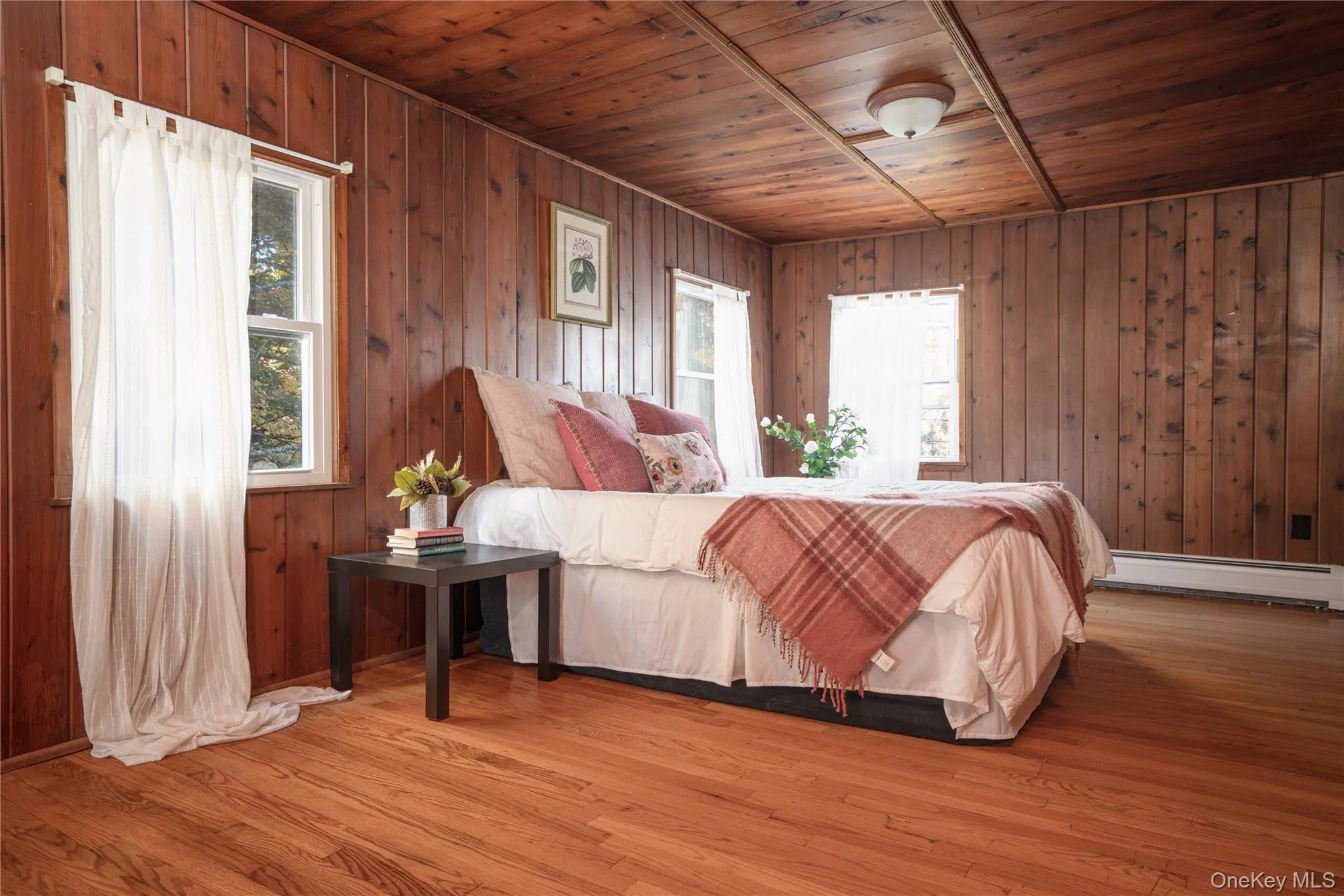 Bedroom with wooden ceiling, wood finished floors, baseboard heating, and wooden walls Bedroom with wooden ceiling, wood finished floors, baseboard heating, and wooden walls