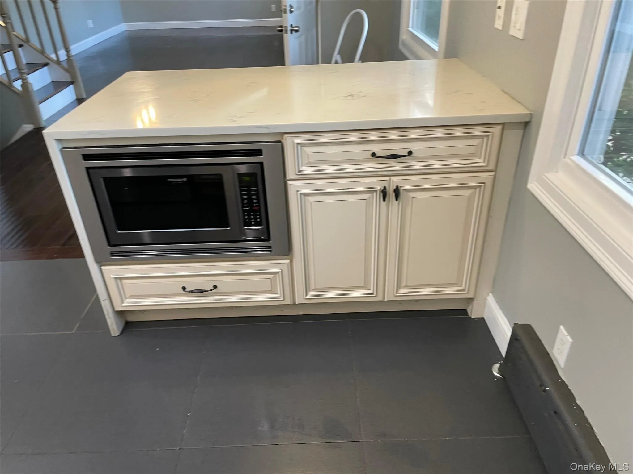 Kitchen featuring dark tile patterned floors, stainless steel microwave, a peninsula, and light stone countertops Kitchen featuring dark tile patterned floors, stainless steel microwave, a peninsula, and light stone countertops