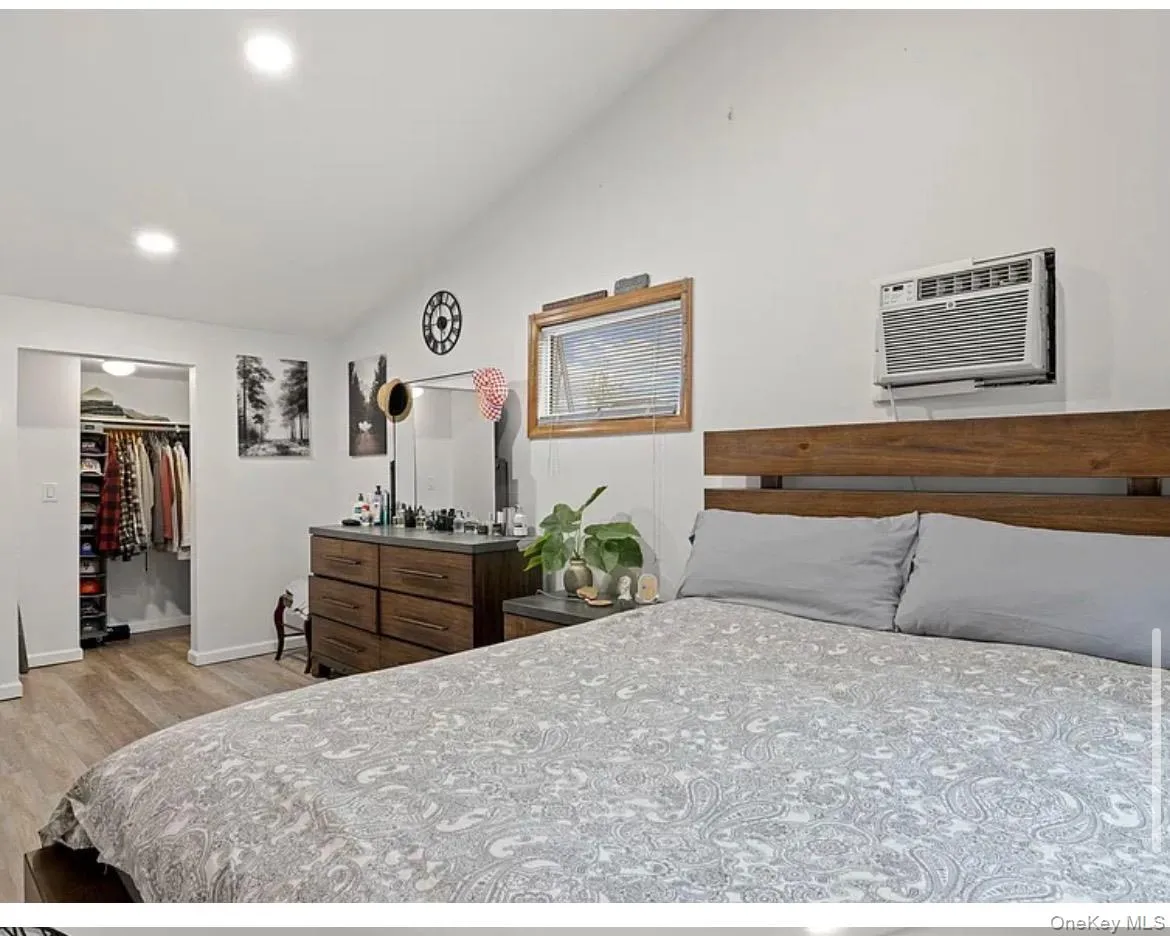 Bedroom with lofted ceiling, a spacious closet, light wood-type flooring, recessed lighting, and a wall mounted air conditioner Bedroom with lofted ceiling, a spacious closet, light wood-type flooring, recessed lighting, and a wall mounted air conditioner