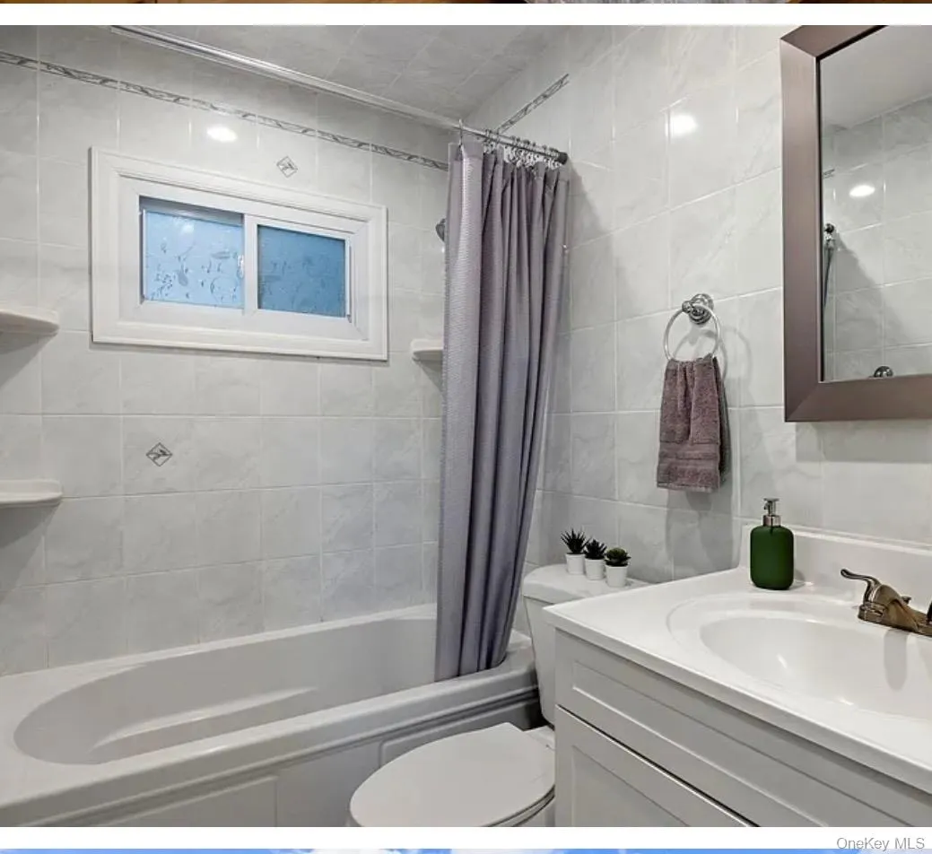 Bathroom with vanity, shower / tub combo with curtain, and tile walls Bathroom with vanity, shower / tub combo with curtain, and tile walls