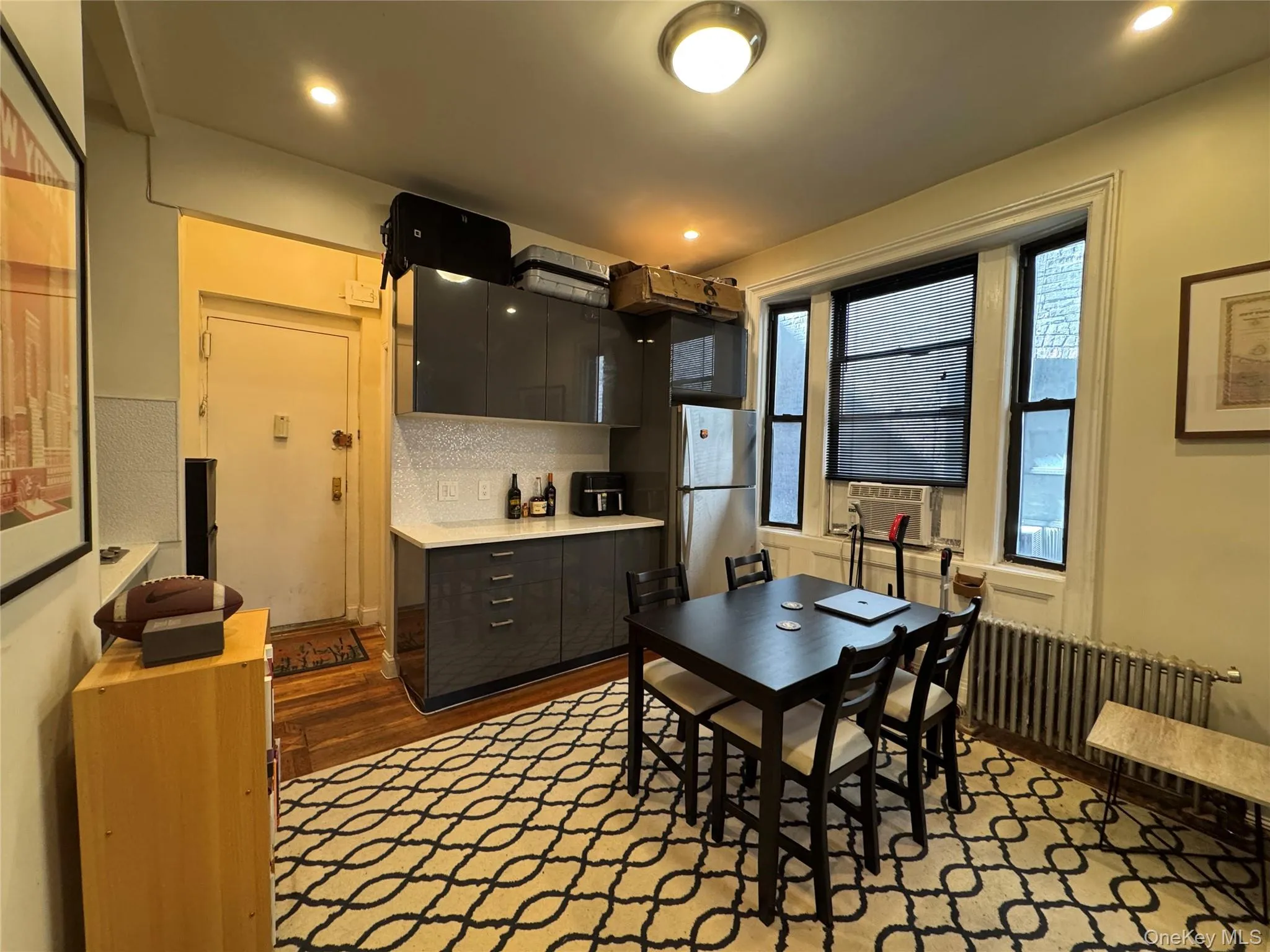 Kitchen featuring dark wood-type flooring, light countertops, decorative backsplash, freestanding refrigerator, and radiator Kitchen featuring dark wood-type flooring, light countertops, decorative backsplash, freestanding refrigerator, and radiator