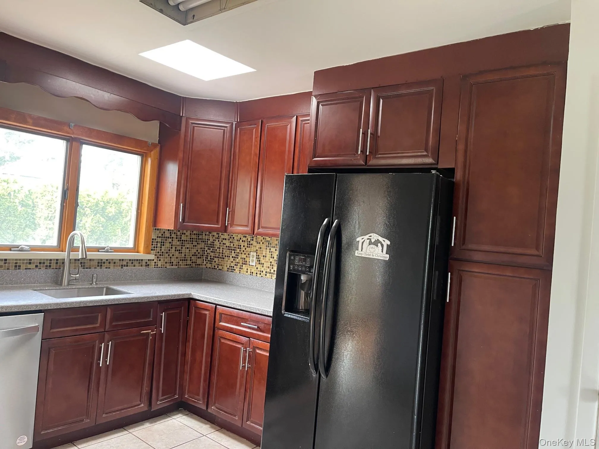 Kitchen featuring black fridge, tasteful backsplash, stainless steel dishwasher, light stone counters, and light tile patterned floors Kitchen featuring black fridge, tasteful backsplash, stainless steel dishwasher, light stone counters, and light tile patterned floors