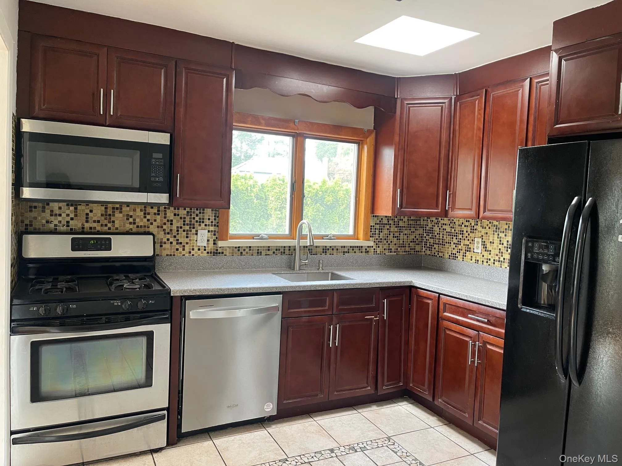 Kitchen with appliances with stainless steel finishes, light tile patterned flooring, backsplash, and dark brown cabinets Kitchen with appliances with stainless steel finishes, light tile patterned flooring, backsplash, and dark brown cabinets