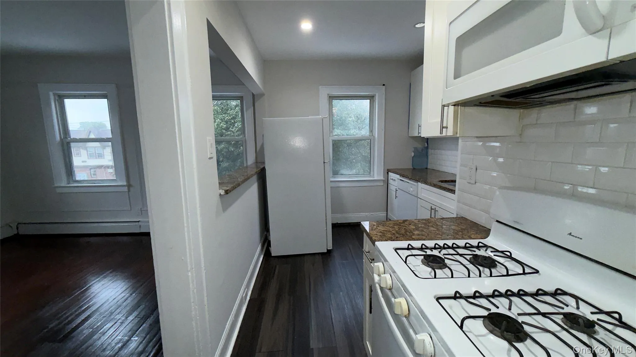 Kitchen with white appliances, white cabinets, dark wood-style floors, and decorative backsplash Kitchen with white appliances, white cabinets, dark wood-style floors, and decorative backsplash