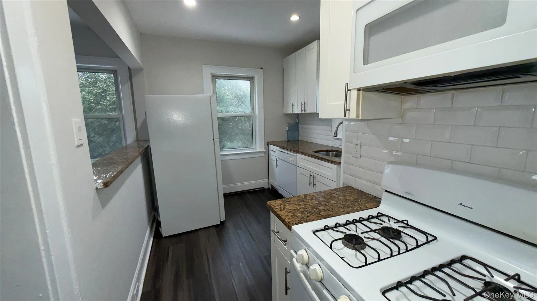 Kitchen featuring white appliances, white cabinets, dark wood-type flooring, backsplash, and recessed lighting Kitchen featuring white appliances, white cabinets, dark wood-type flooring, backsplash, and recessed lighting