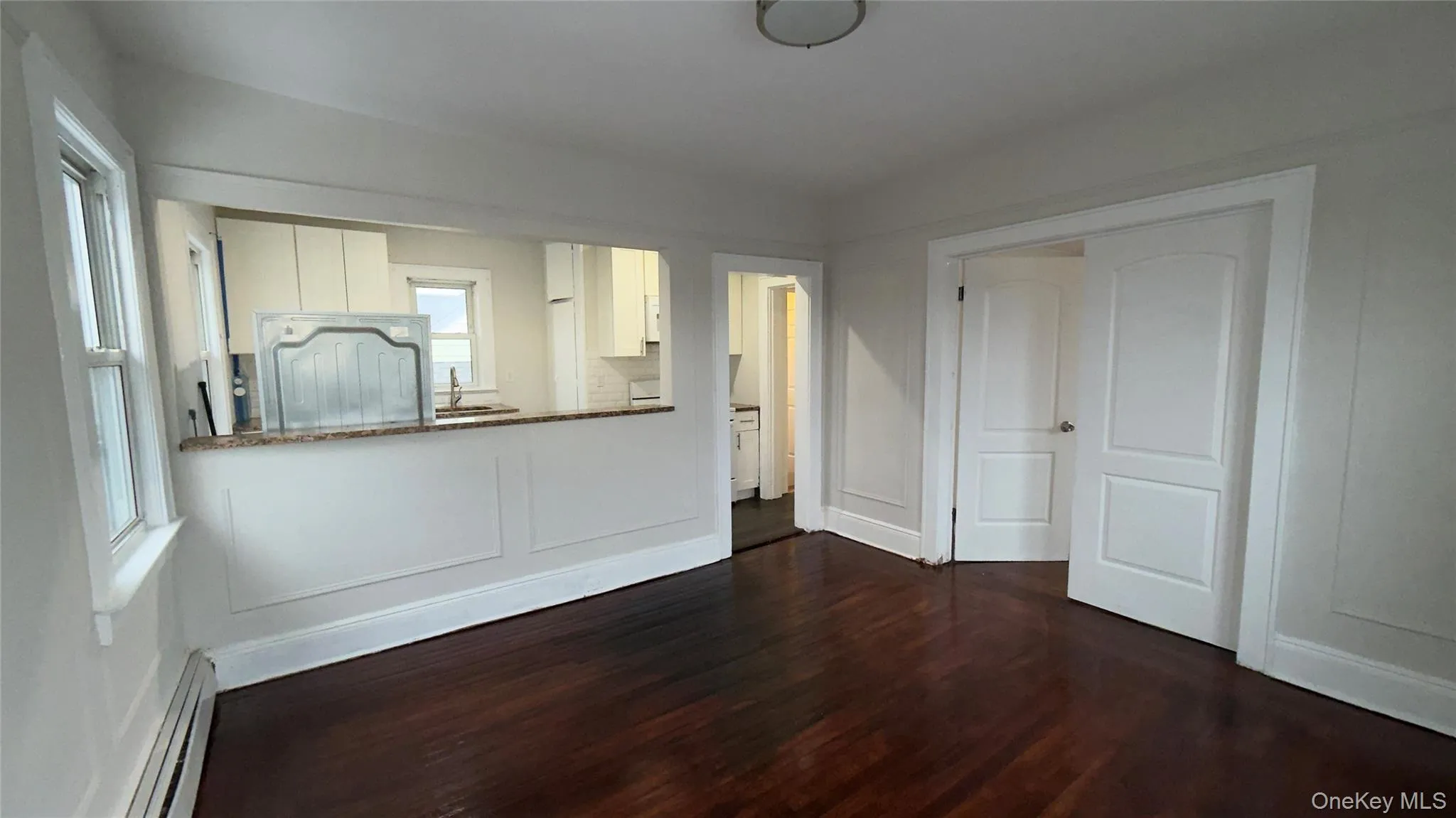 Kitchen featuring white cabinetry, dark wood-style floors, a baseboard heating unit, dark stone counters, and refrigerator Kitchen featuring white cabinetry, dark wood-style floors, a baseboard heating unit, dark stone counters, and refrigerator