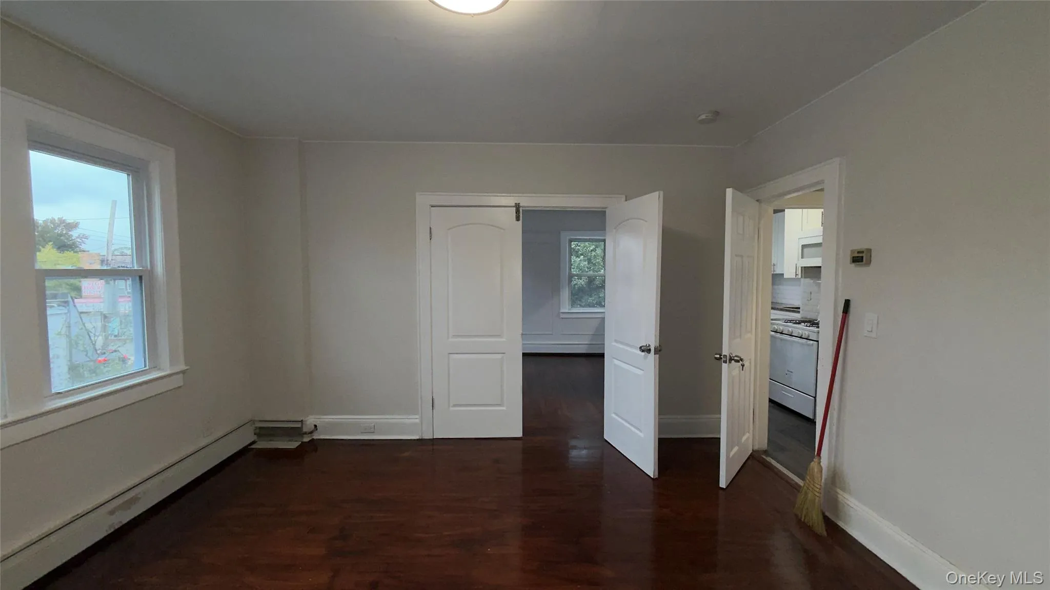 Unfurnished room with baseboard heating and dark wood finished floors Unfurnished room with baseboard heating and dark wood finished floors