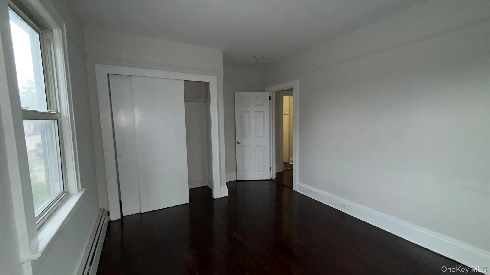 Unfurnished bedroom with dark wood-type flooring, a baseboard heating unit, and a closet Unfurnished bedroom with dark wood-type flooring, a baseboard heating unit, and a closet