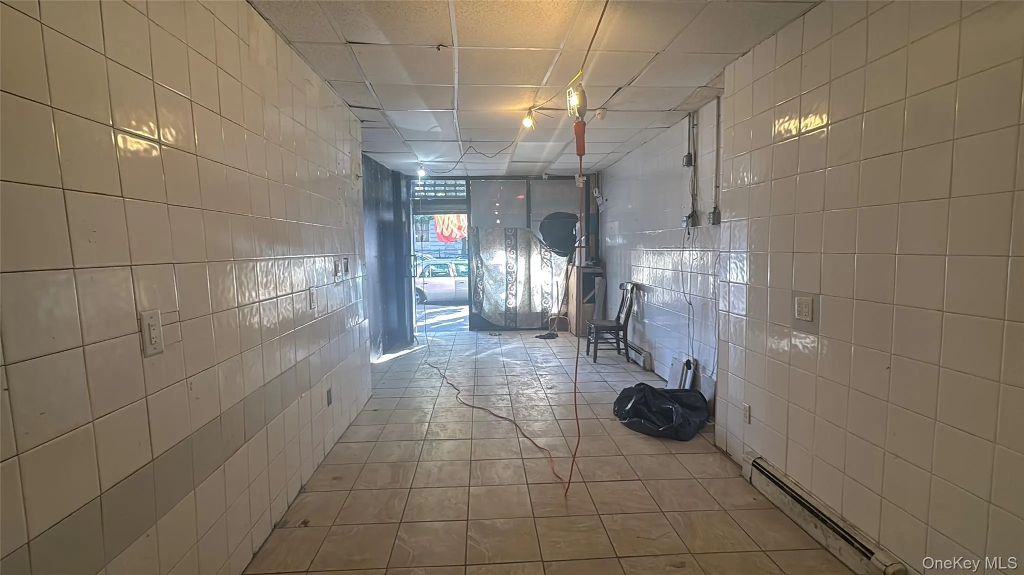 Hallway featuring tile walls, baseboard heating, a drop ceiling, and tile patterned floors Hallway featuring tile walls, baseboard heating, a drop ceiling, and tile patterned floors